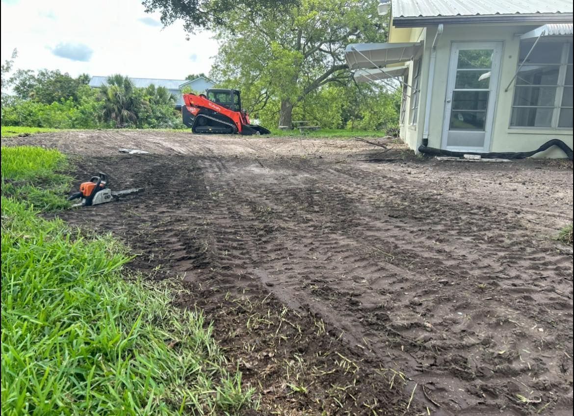 A tractor is driving down a dirt road in front of a house.