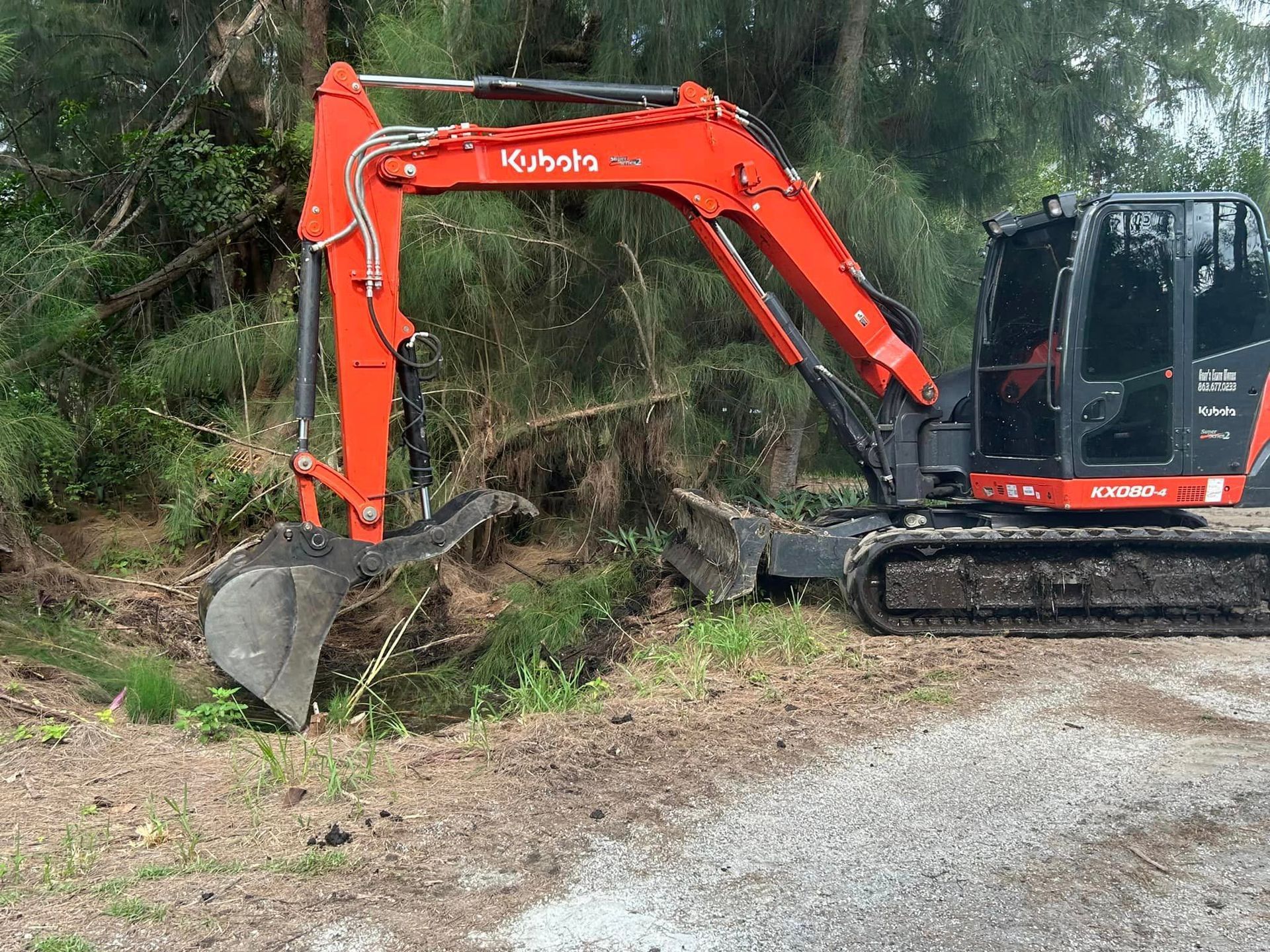 A red and black excavator is sitting on the side of a dirt road.