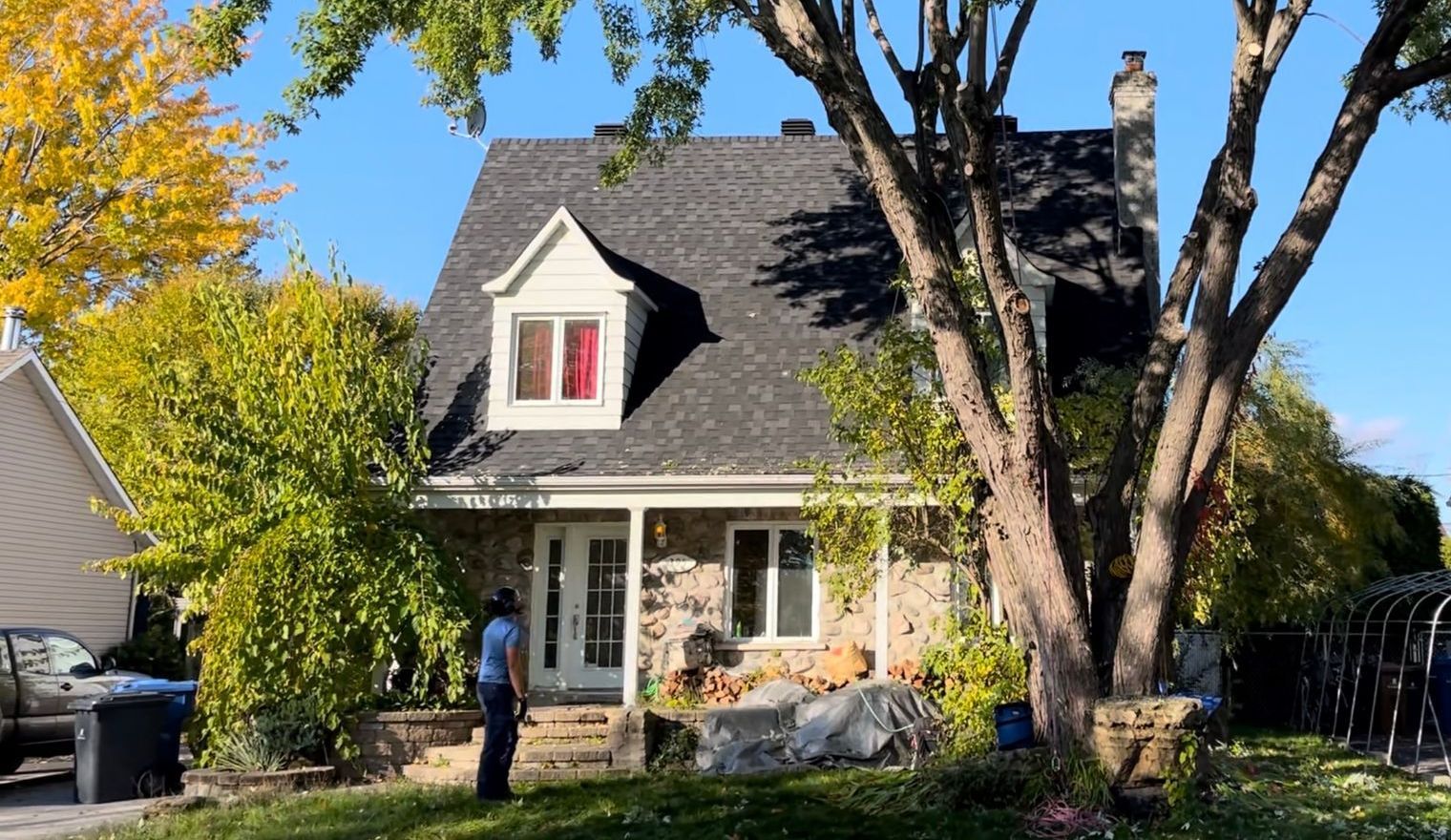 Maison en pierre au toit noir et lucarne. Une personne se tient sur des marches.