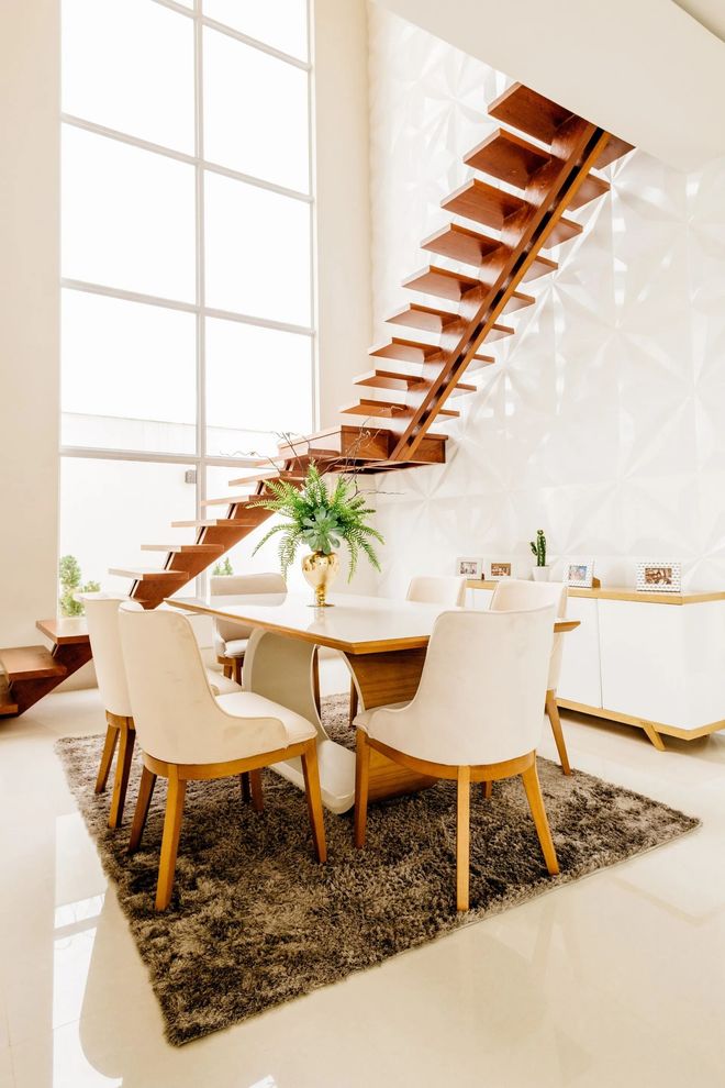 Modern dining area with a wooden staircase, round table, and beige chairs in a bright white interior