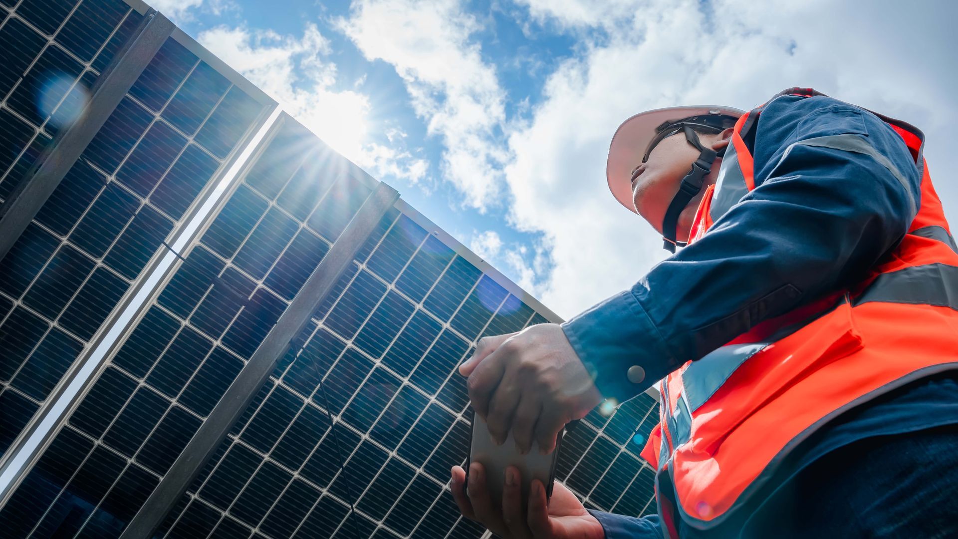 A man in an orange vest is working on a solar panel.