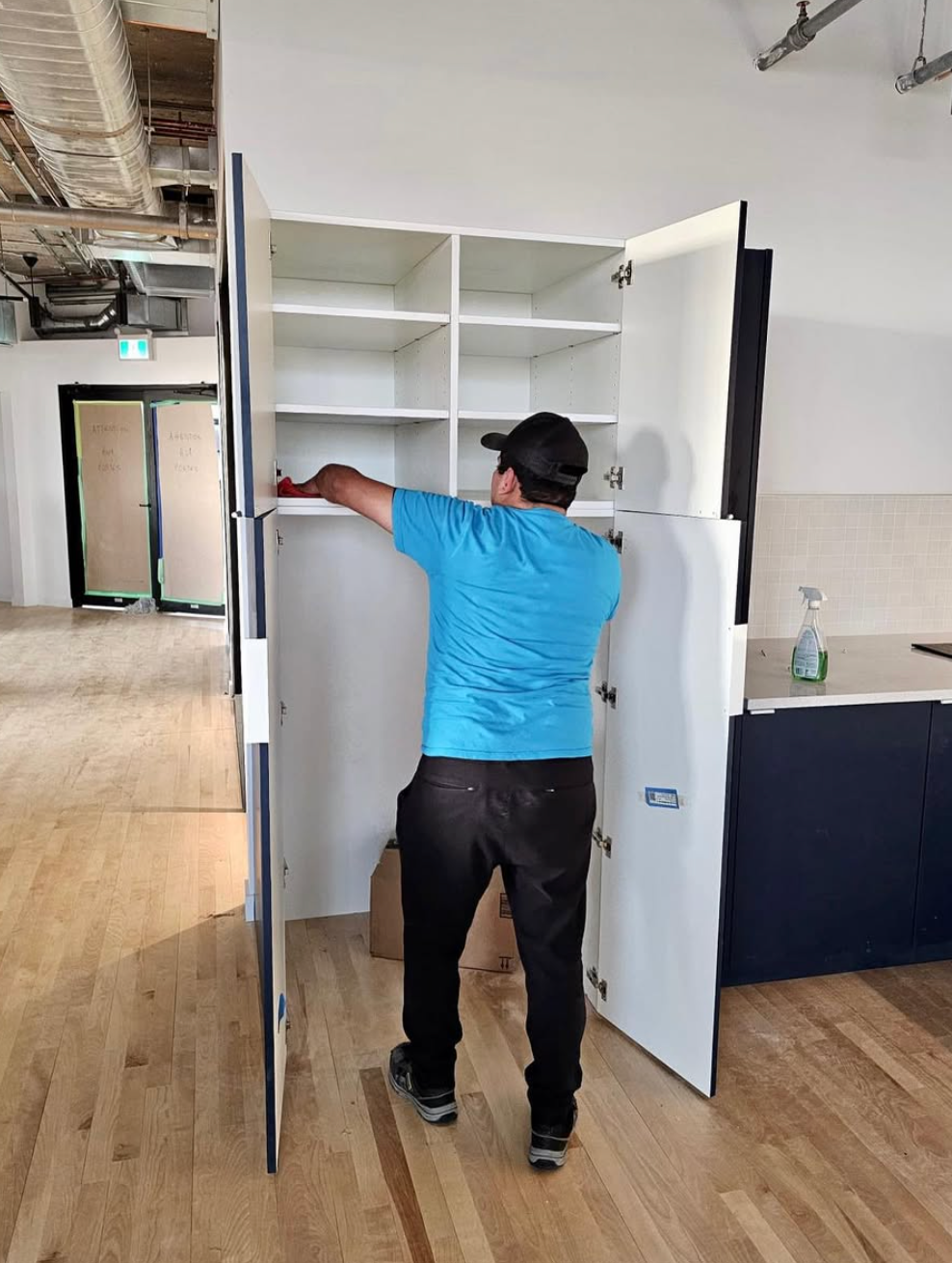 Une personne ouvre les portes d'un placard dans une pièce avec parquet et une kitchenette.