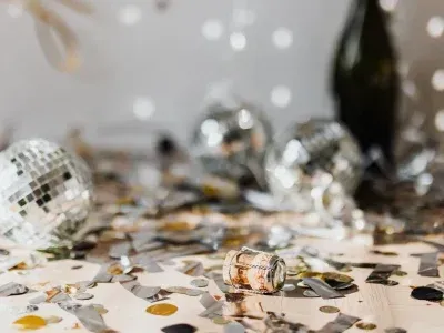 Boules disco, confettis et bouchon de champagne sur une table, célébrant une occasion festive.