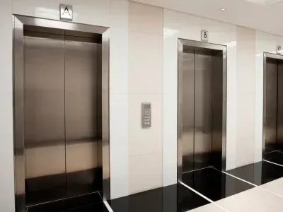 Dans un immeuble moderne, trois portes d'ascenseur en acier inoxydable, étiquetées A, B et C.