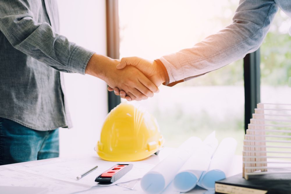 Two People Shaking Hands Over a Desk With Blueprints — Search Partners in Melbourne, VIC