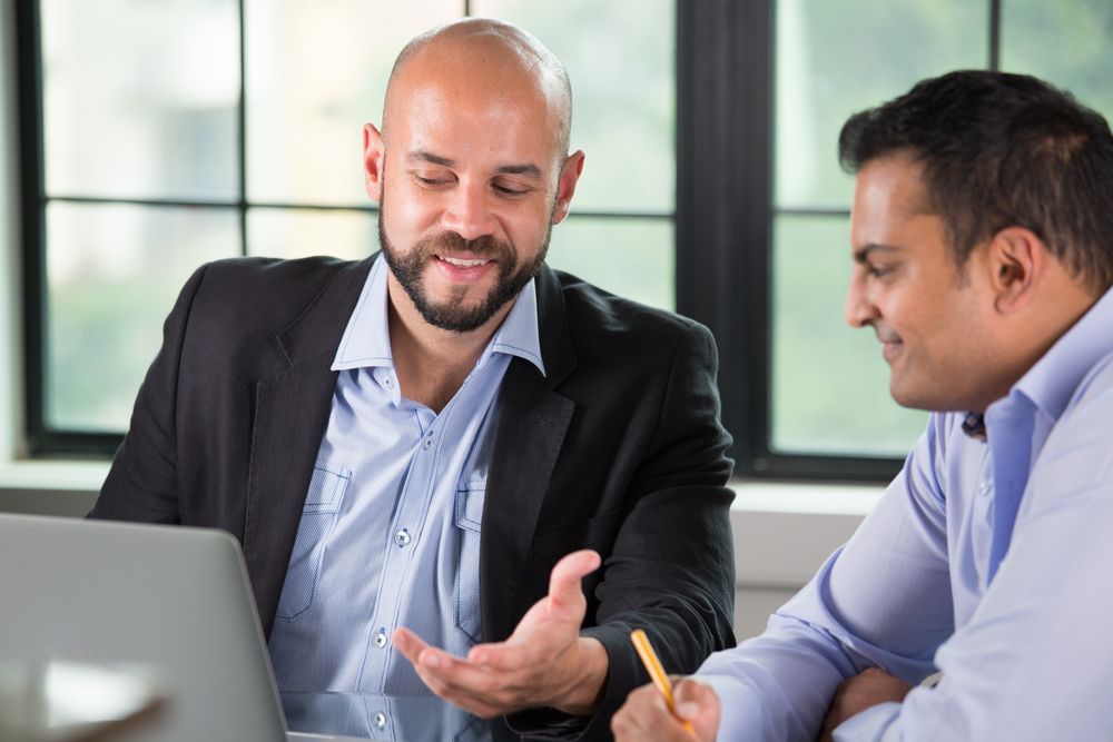 Two coworkers smiling and discussing something at a laptop in an office setting — Search Partners in Melbourne, VIC