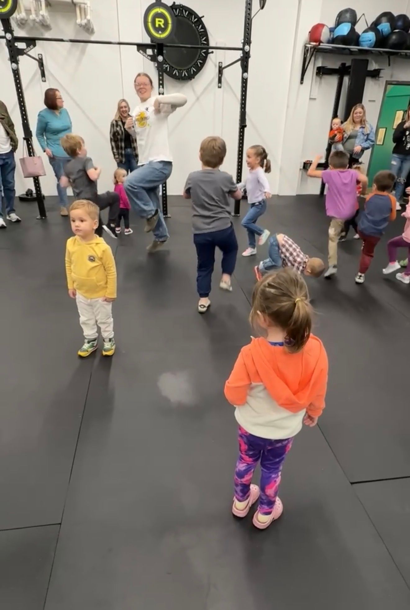 Children exercising in a gym, with a coach leading a group workout on padded flooring at Everyday Strength, a gym in Wenatchee, WA
