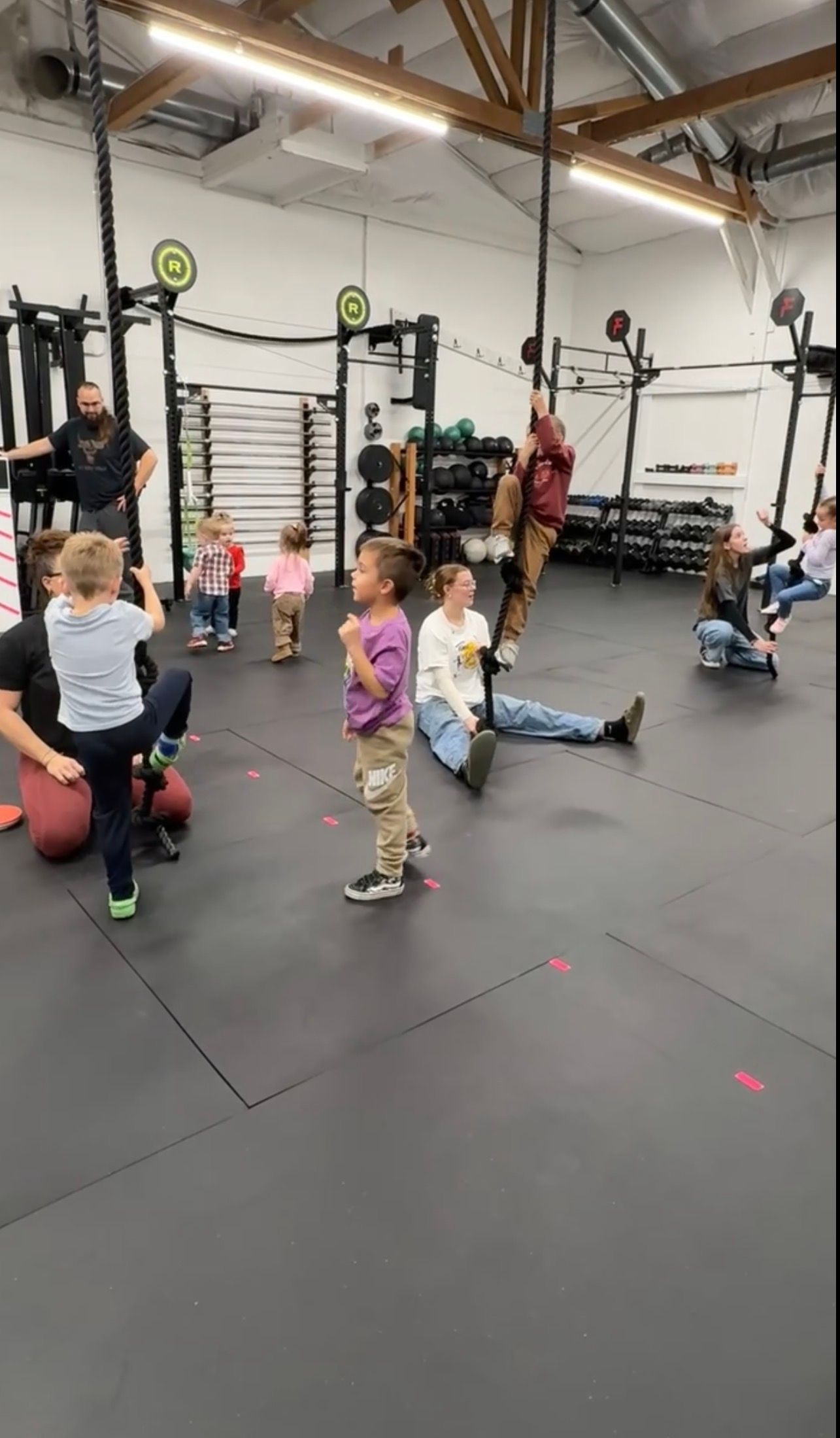 People exercising in Everyday Strength, a gym in Wenatchee, WA, doing floor workouts on black mats with kettlebells and pull-up rigs nearby.