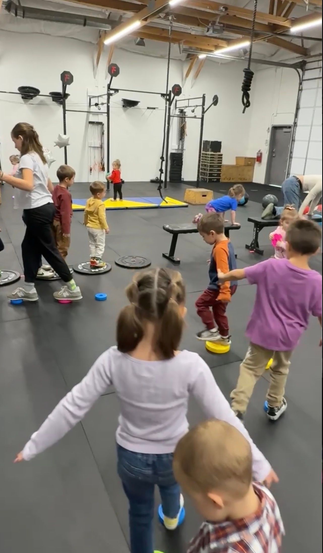 Children stretching with an instructor in a gym studio, standing around a marked floor area at Everyday Strength, a gym in Wenatchee, WA