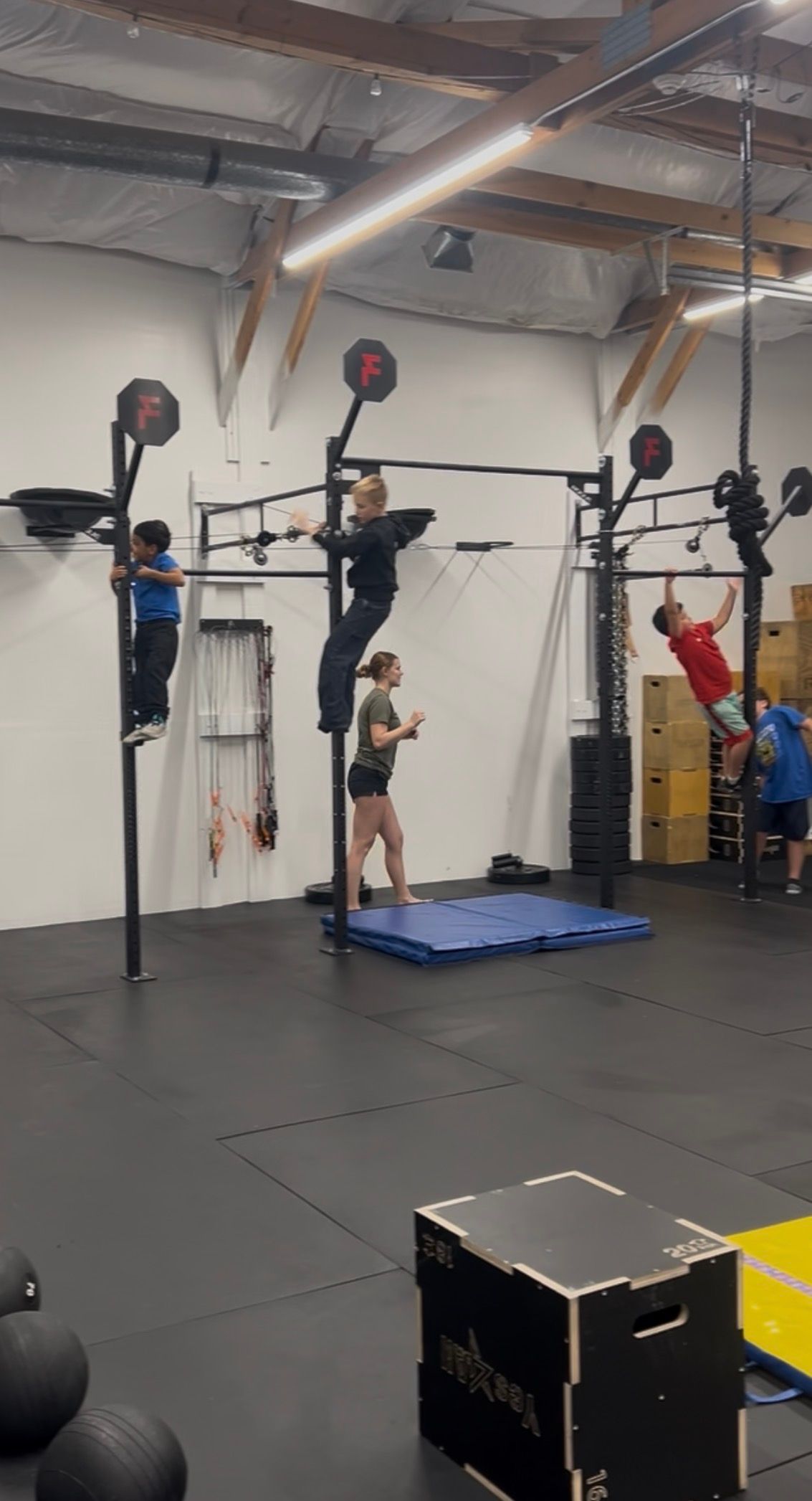 Everyday Strength, a gym in Wenatchee, WA with three people doing pull-ups on rigs over blue mats, and a box in the foreground