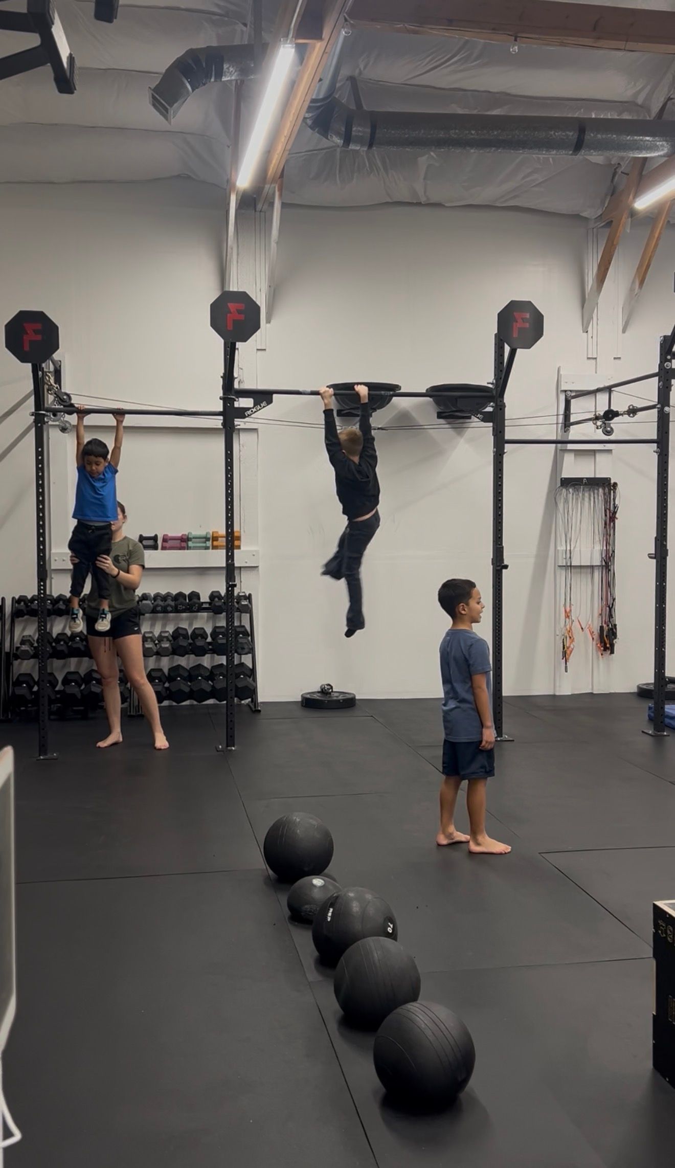People training on pull-up rigs in Everyday Strength, a gym in Wenatchee, WA, with medicine balls lined up on the floor.