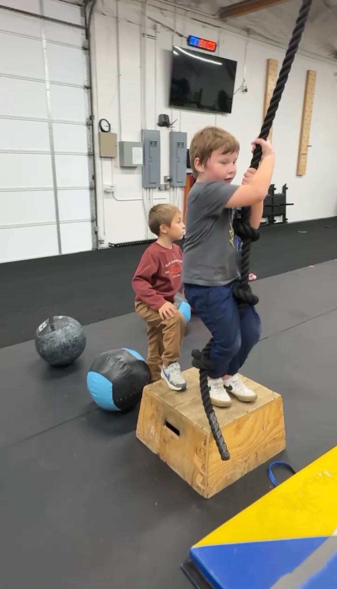 Two children balancing on wooden boxes in Everyday Strength, a gym in Wenatchee, WA, with exercise balls nearby.