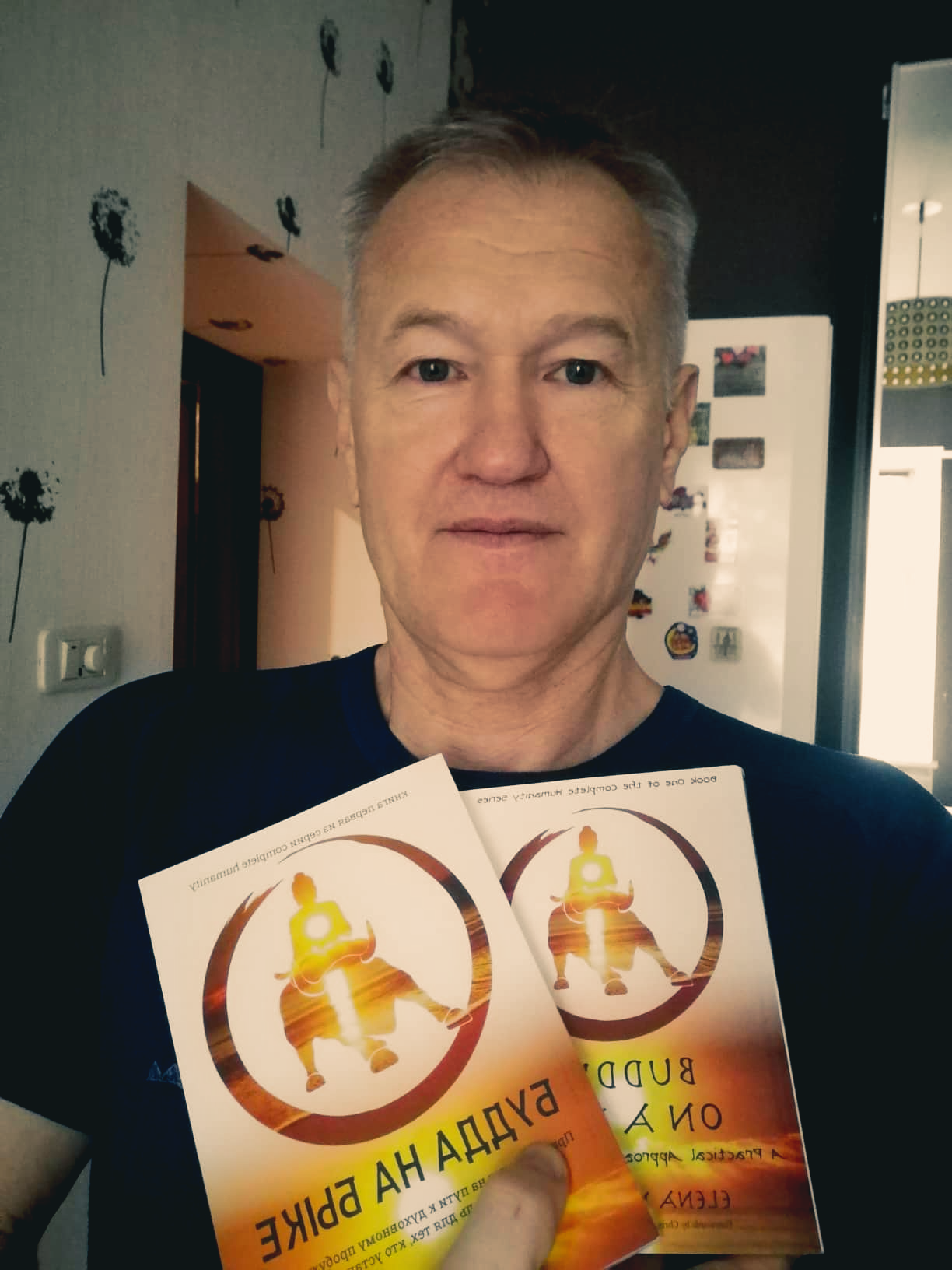 Man holding two books with a circular design, smiling indoors.