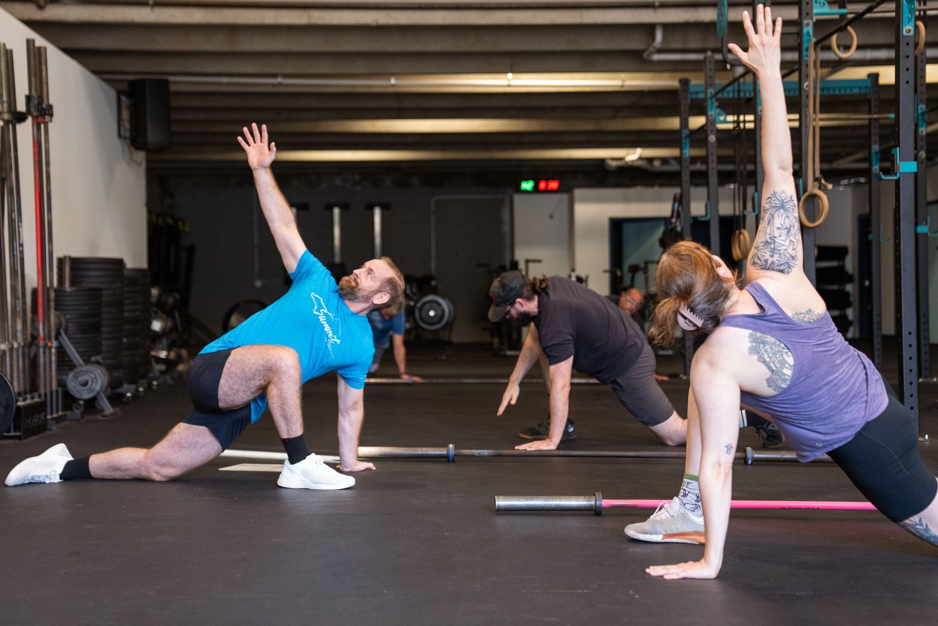 Man in gym in Asheville, NC, lifting kettlebell overhead, other person in background, both wearing activewear.