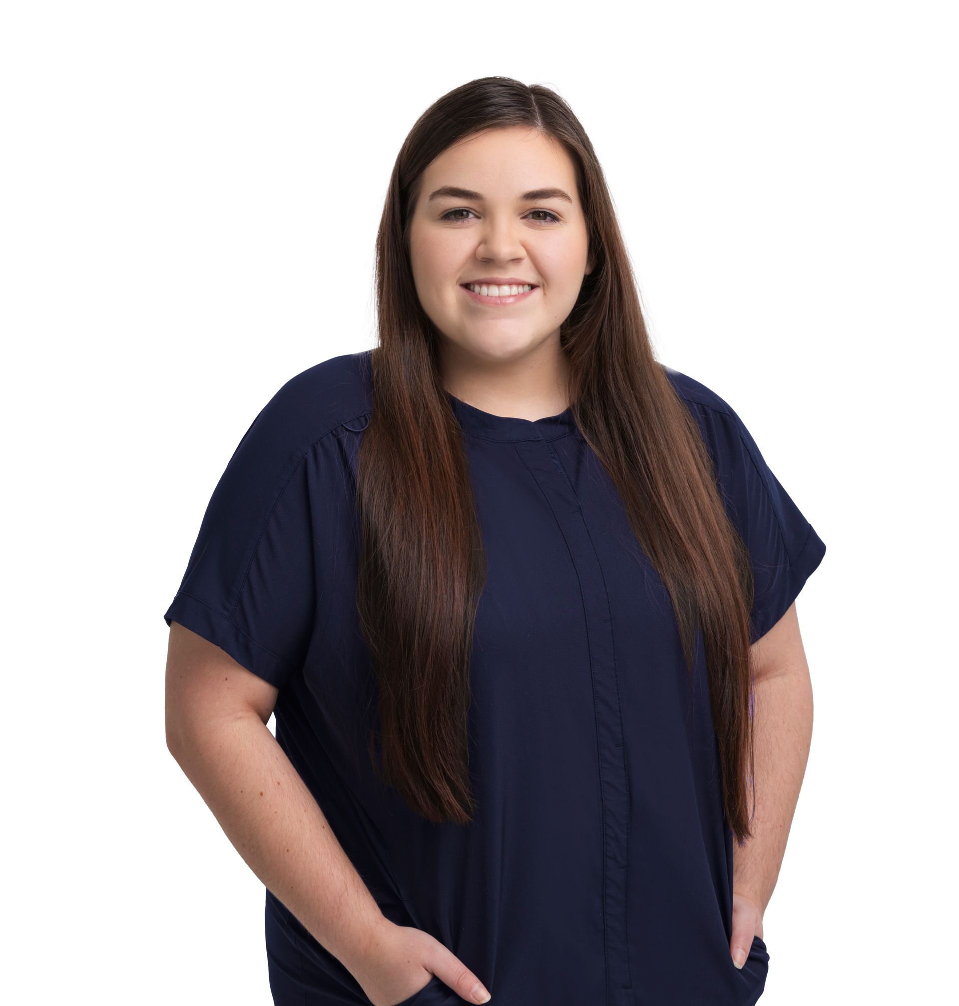 Woman standing against a white background, wearing a navy top and smiling with hands in pockets