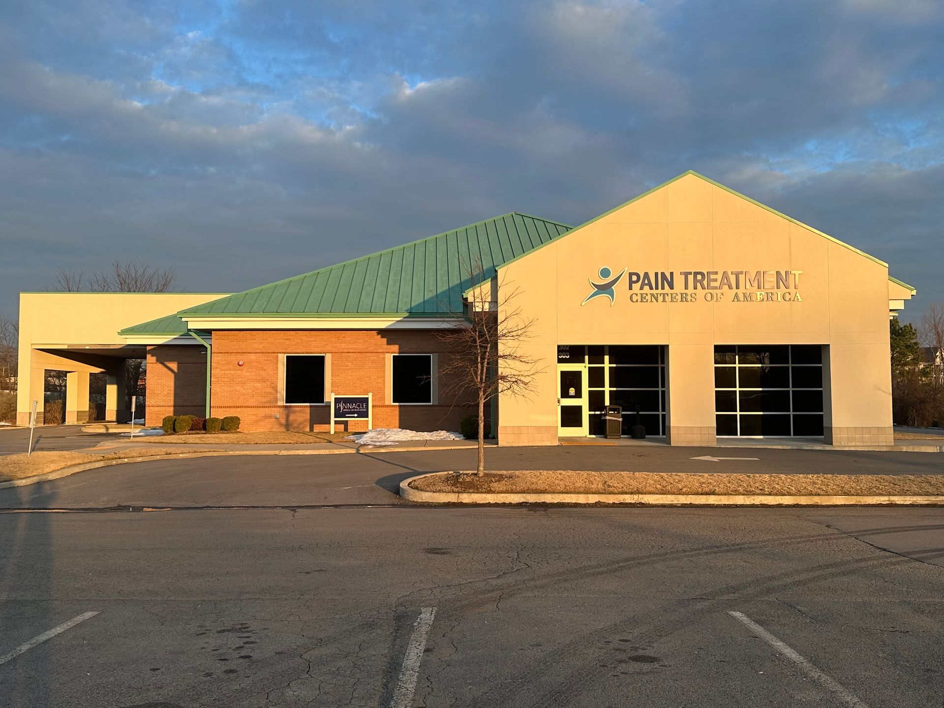Commercial building with green roof and beige facade at sunset, parking lot in front