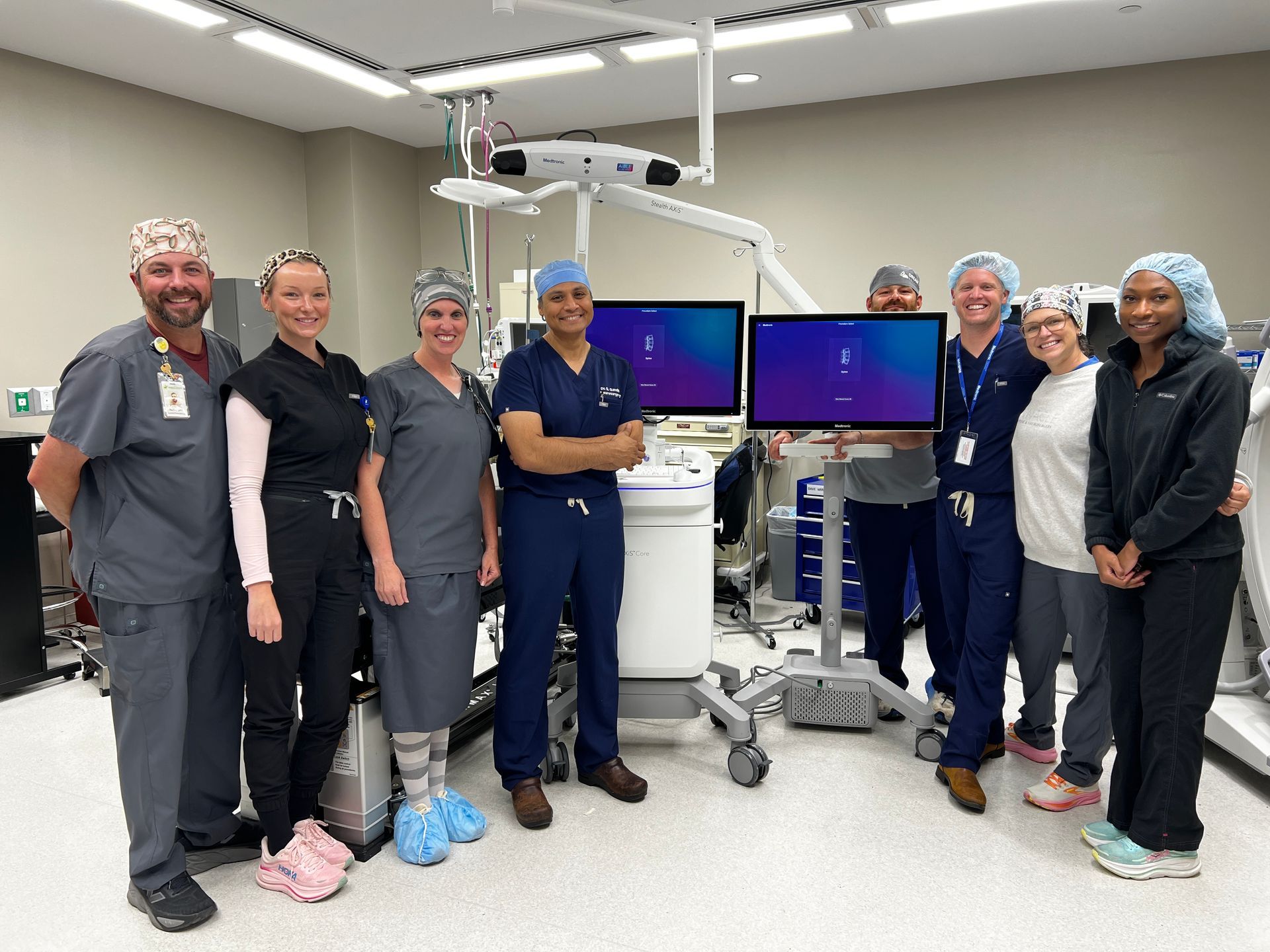 Surgical staff, including, Dr. Gandhi, standing in a medical room beside the Stealth AXis Surgical System.