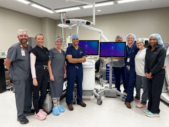 Surgical staff, including, Dr. Gandhi, standing in a medical room beside the Stealth AXis Surgical System.