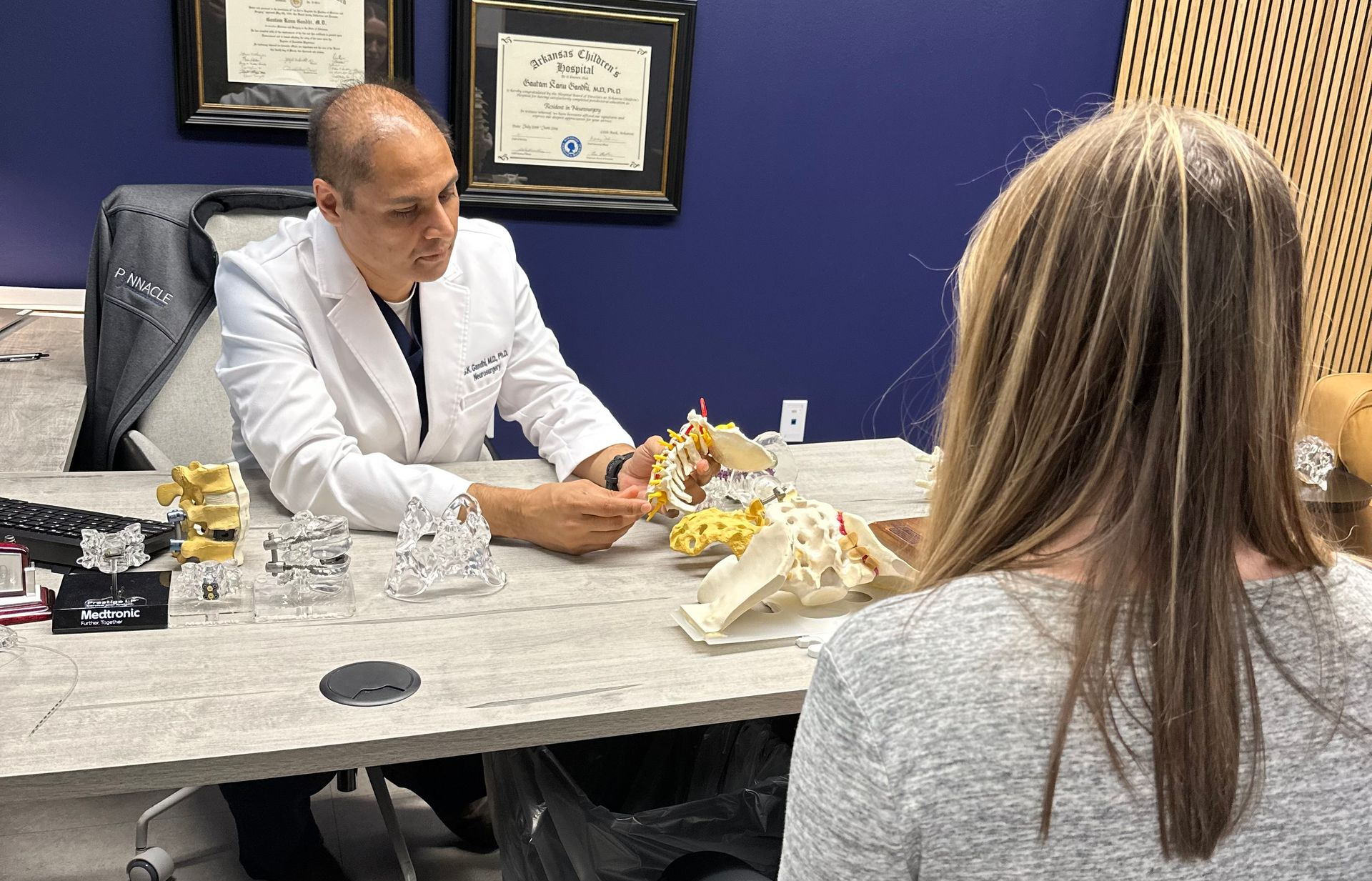 Doctor examining a patient in a clinic office, with medical charts on the wall.