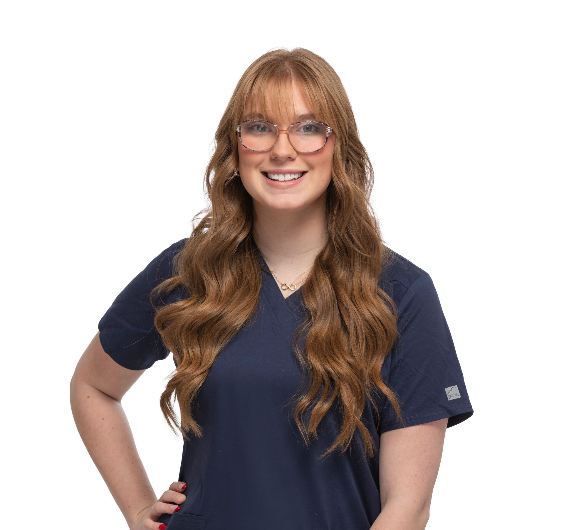 Smiling person with long wavy hair and glasses wearing navy scrubs on a white background