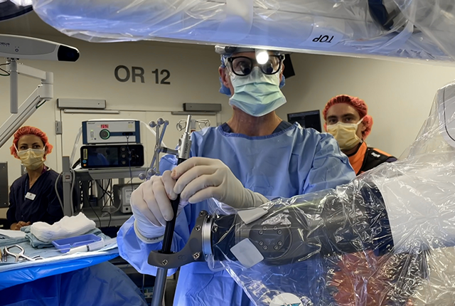Surgeons in an operating room performing a procedure, viewed through clear protective drapes.