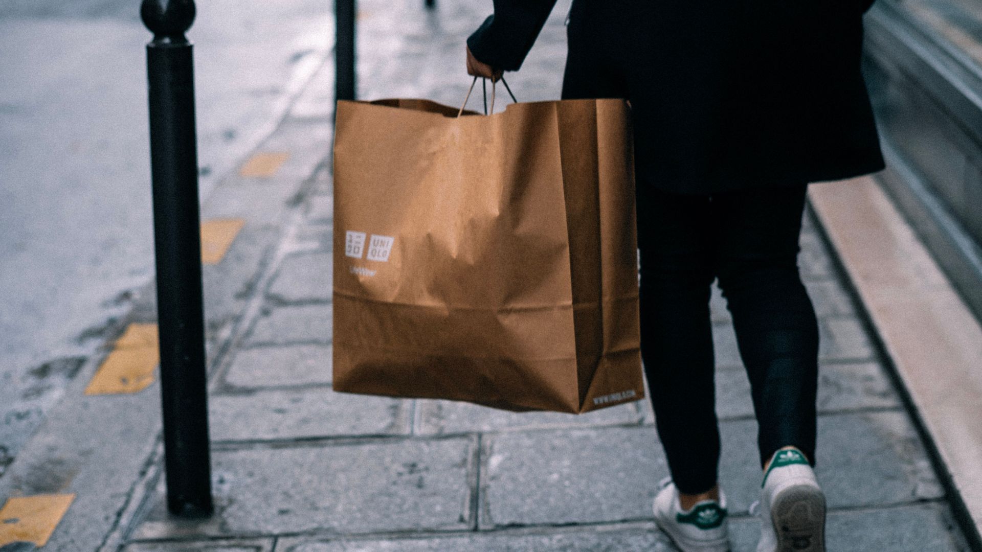 Person walking on a sidewalk carrying a brown paper shopping bag