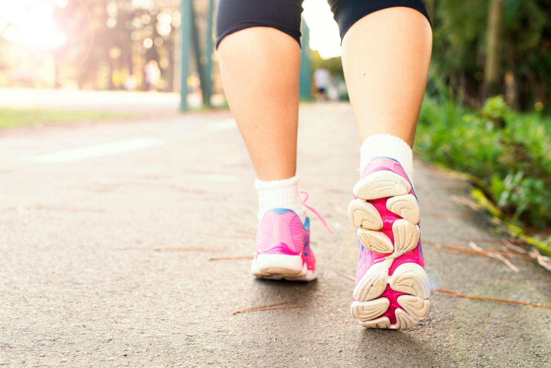 Close-up of a person walking on a paved path in pink sneakers and black shorts