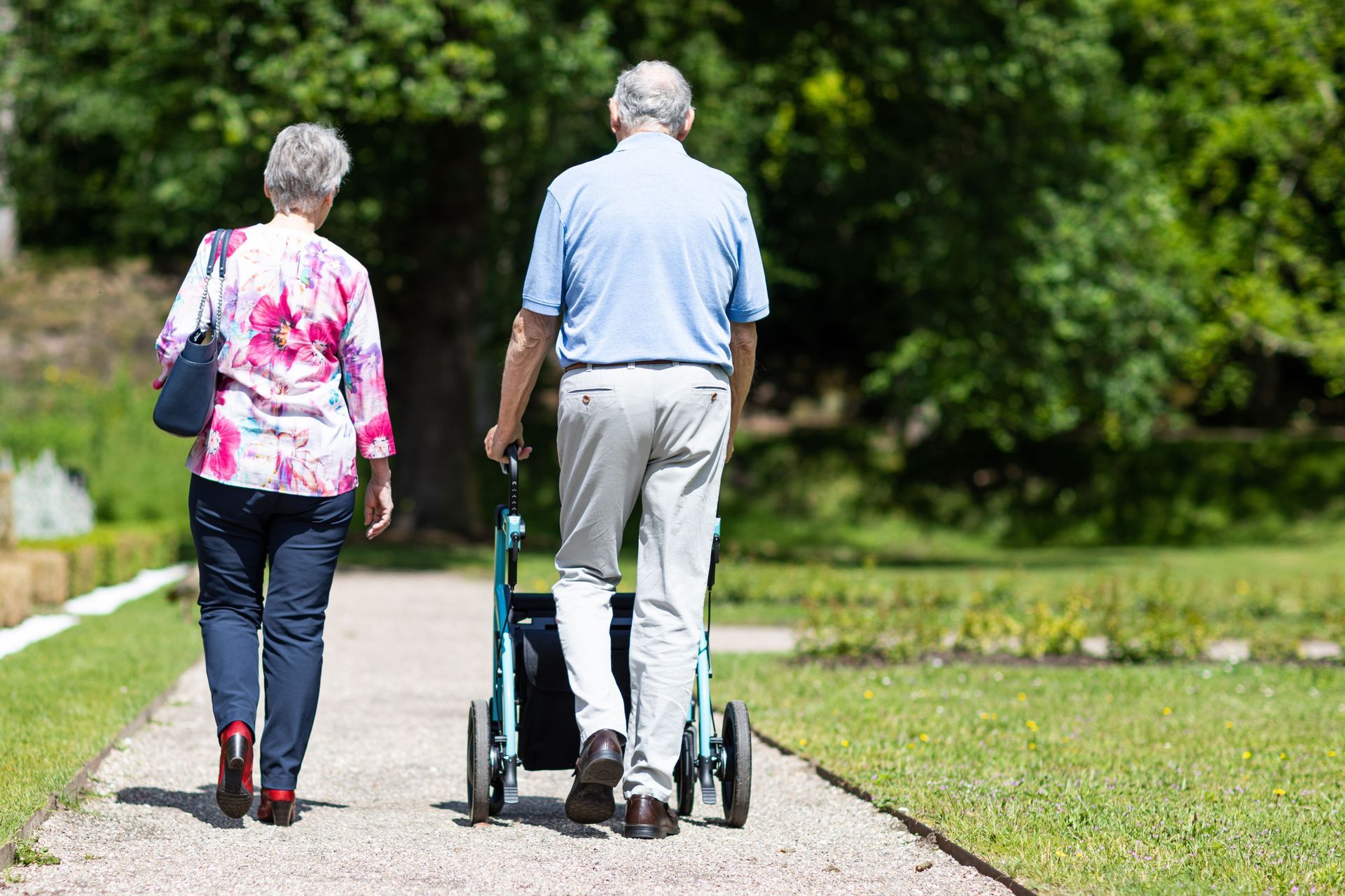 Two people walking away on a path, one using a rollator in a green park