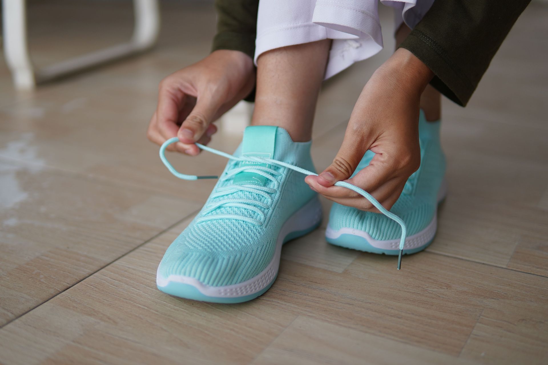 Hands tying the laces of aqua blue sneakers on a wooden floor