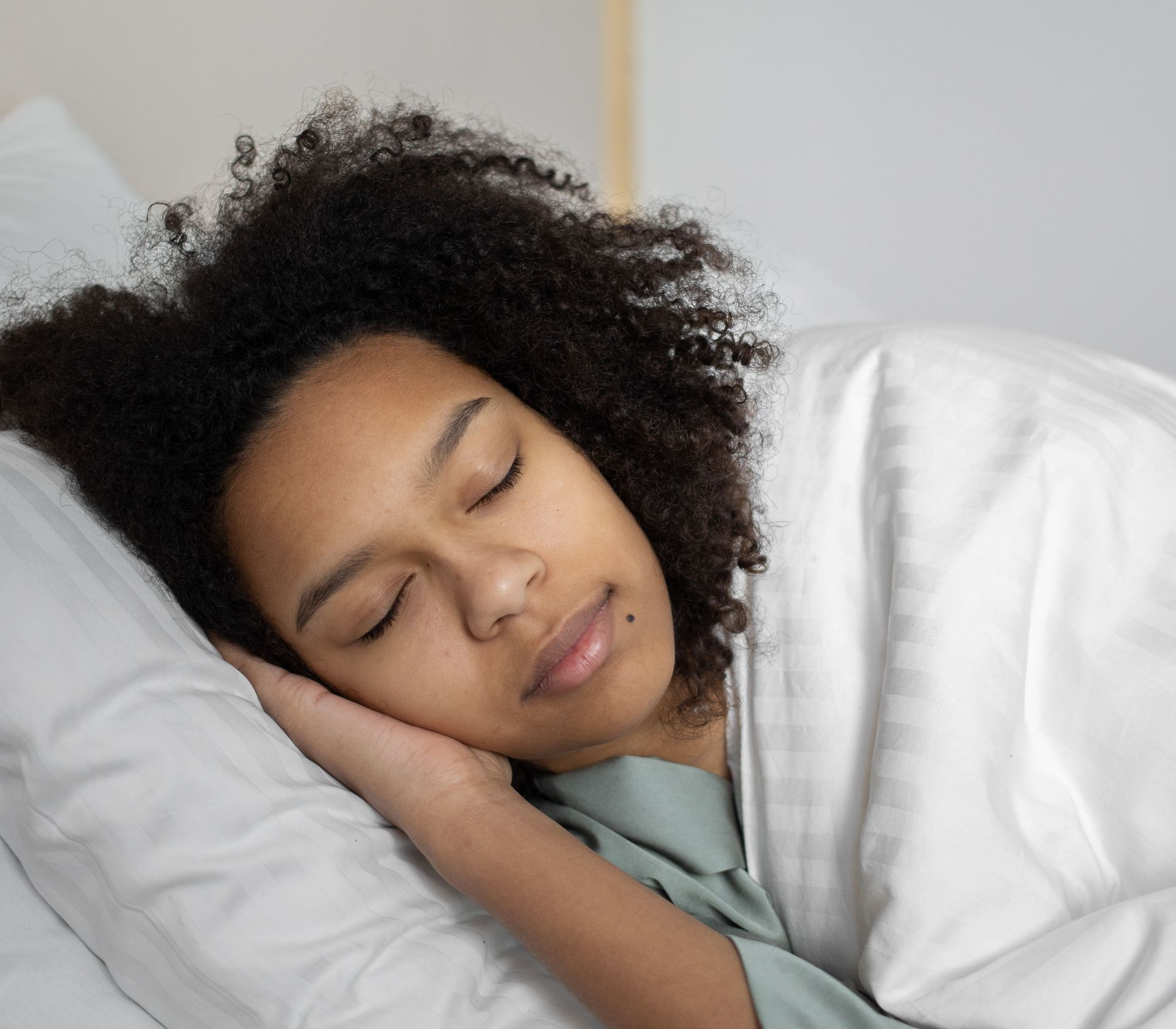 Person sleeping peacefully in bed with white bedding, head resting on a pillow.