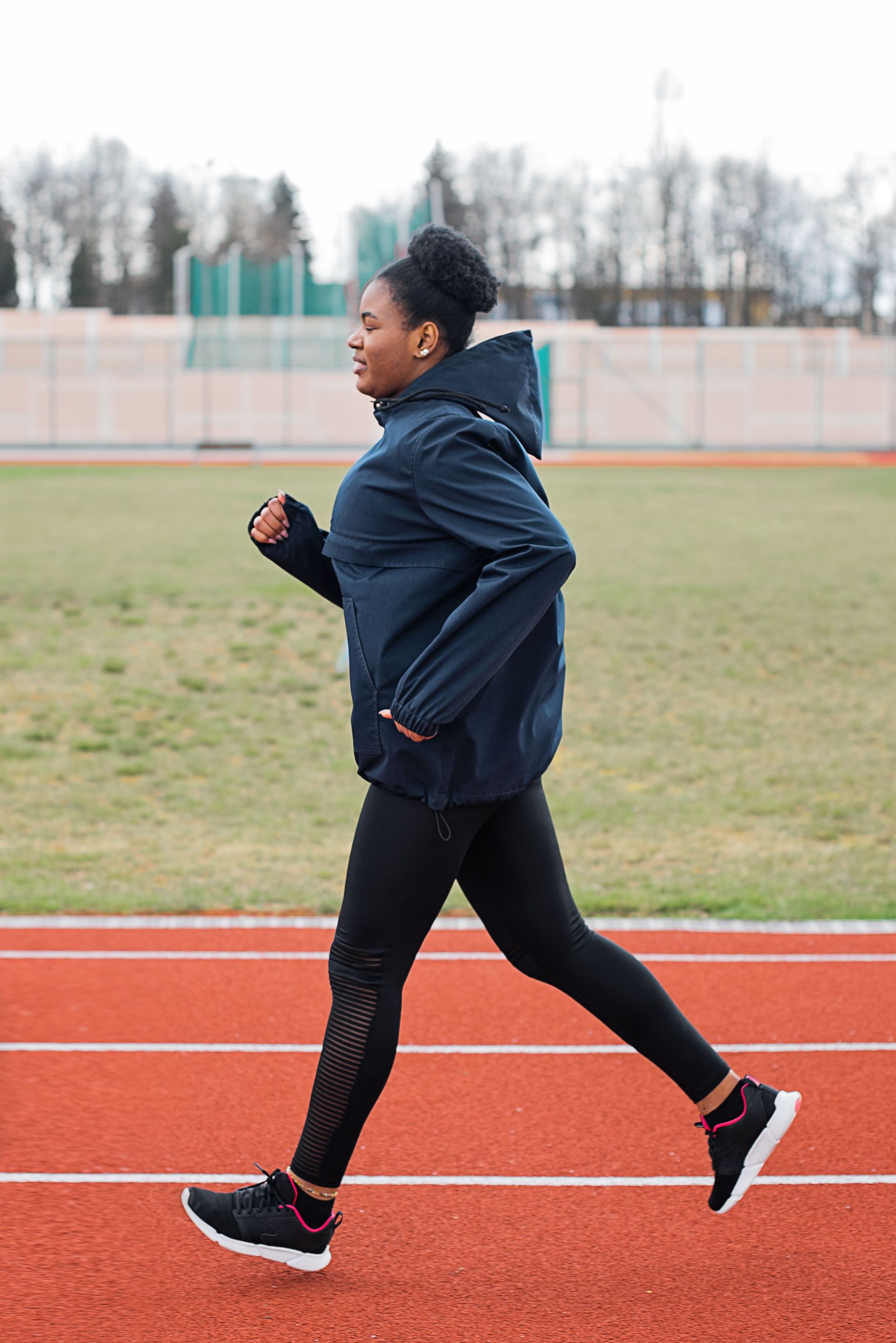 Woman jogging on an outdoor track in a navy jacket and black leggings.