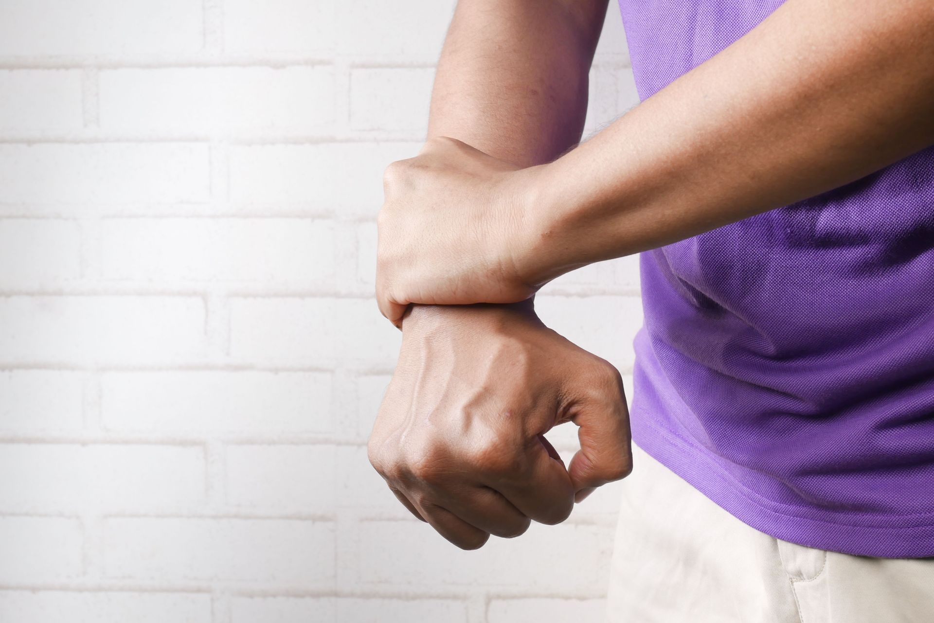 Close-up of a person clutching their forearm in pain against a white brick wall