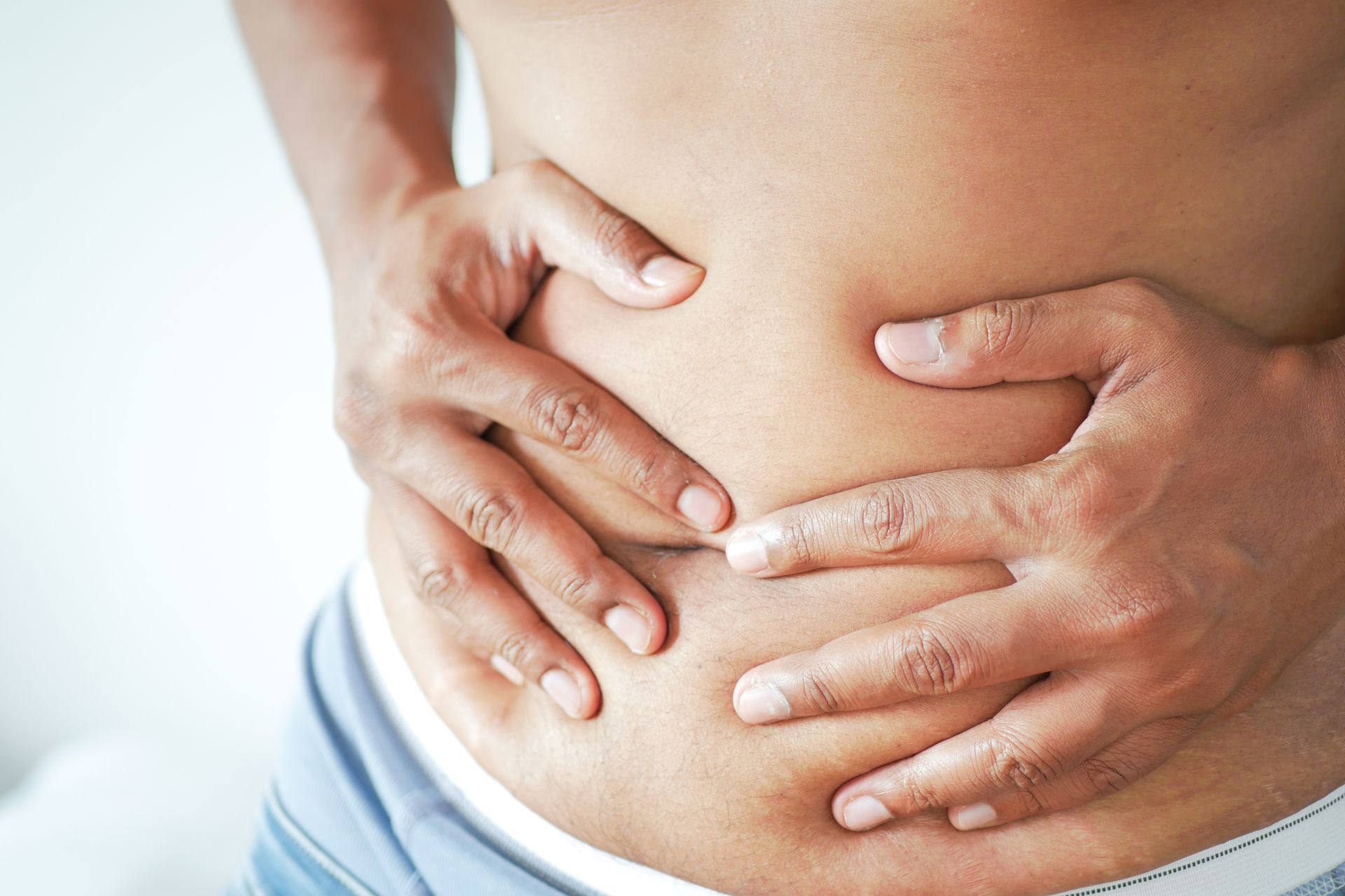 Man holding his stomach in pain, showing visible belly fat.
