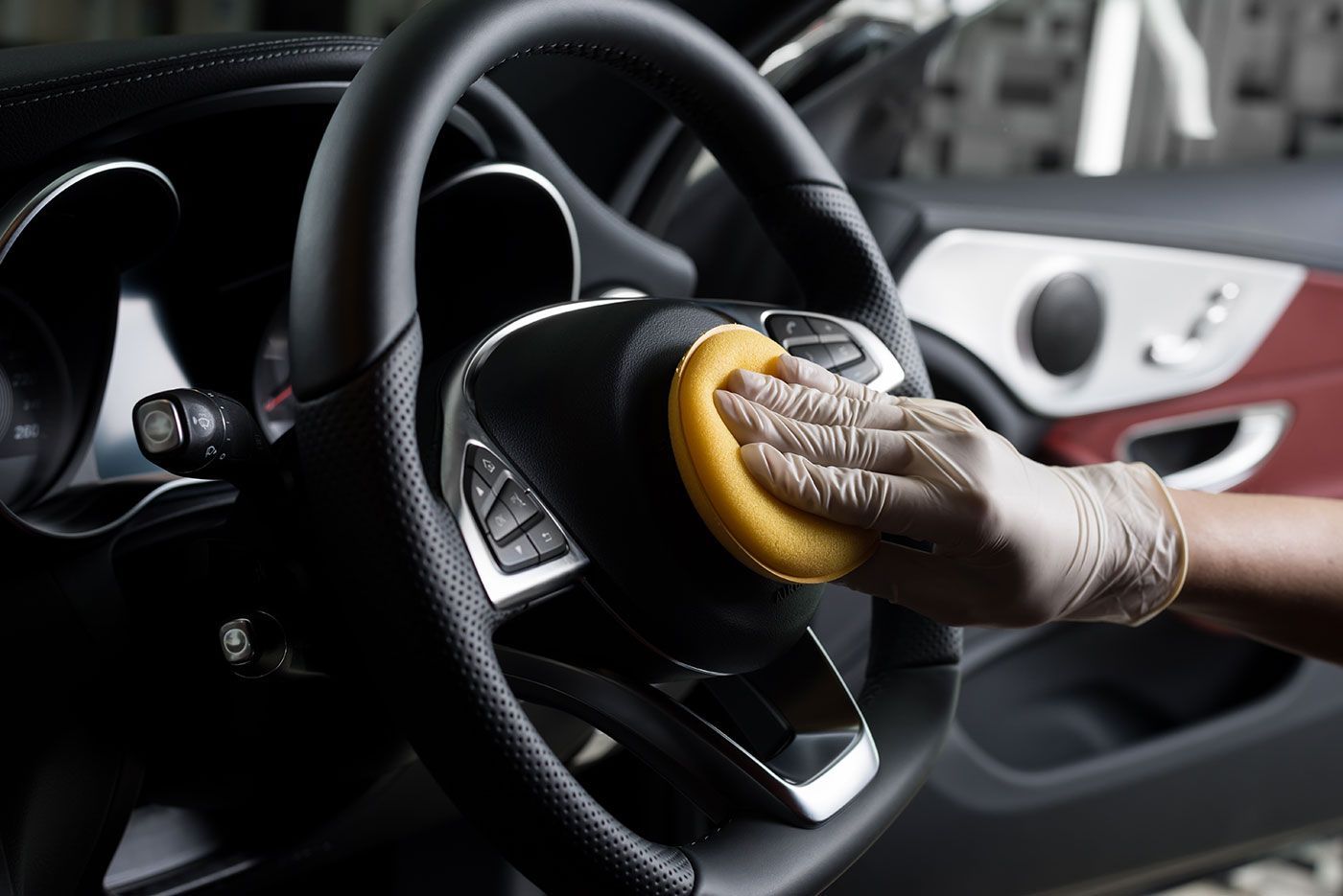 A person is cleaning the steering wheel of a car with a sponge.