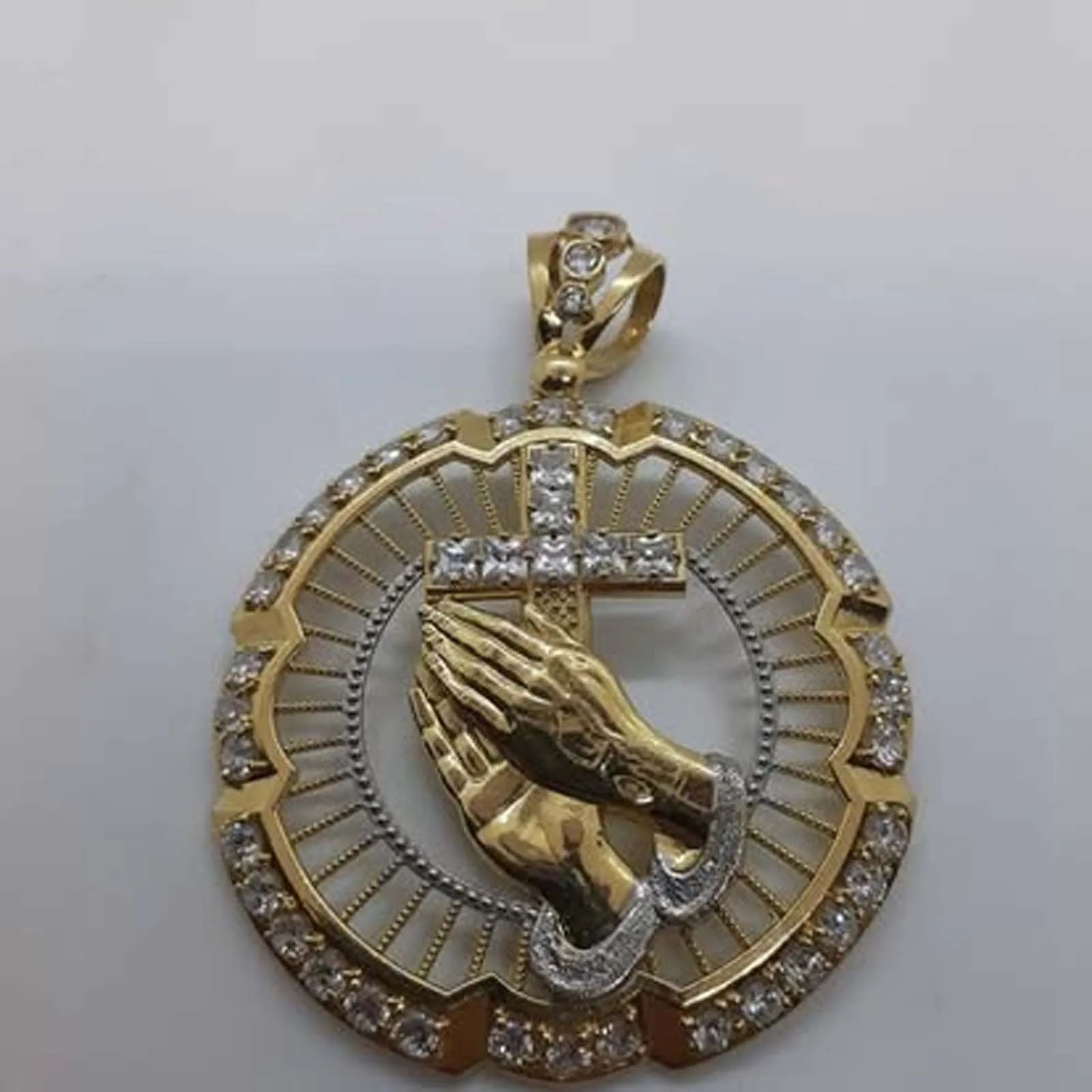 A gold pendant with praying hands and a cross