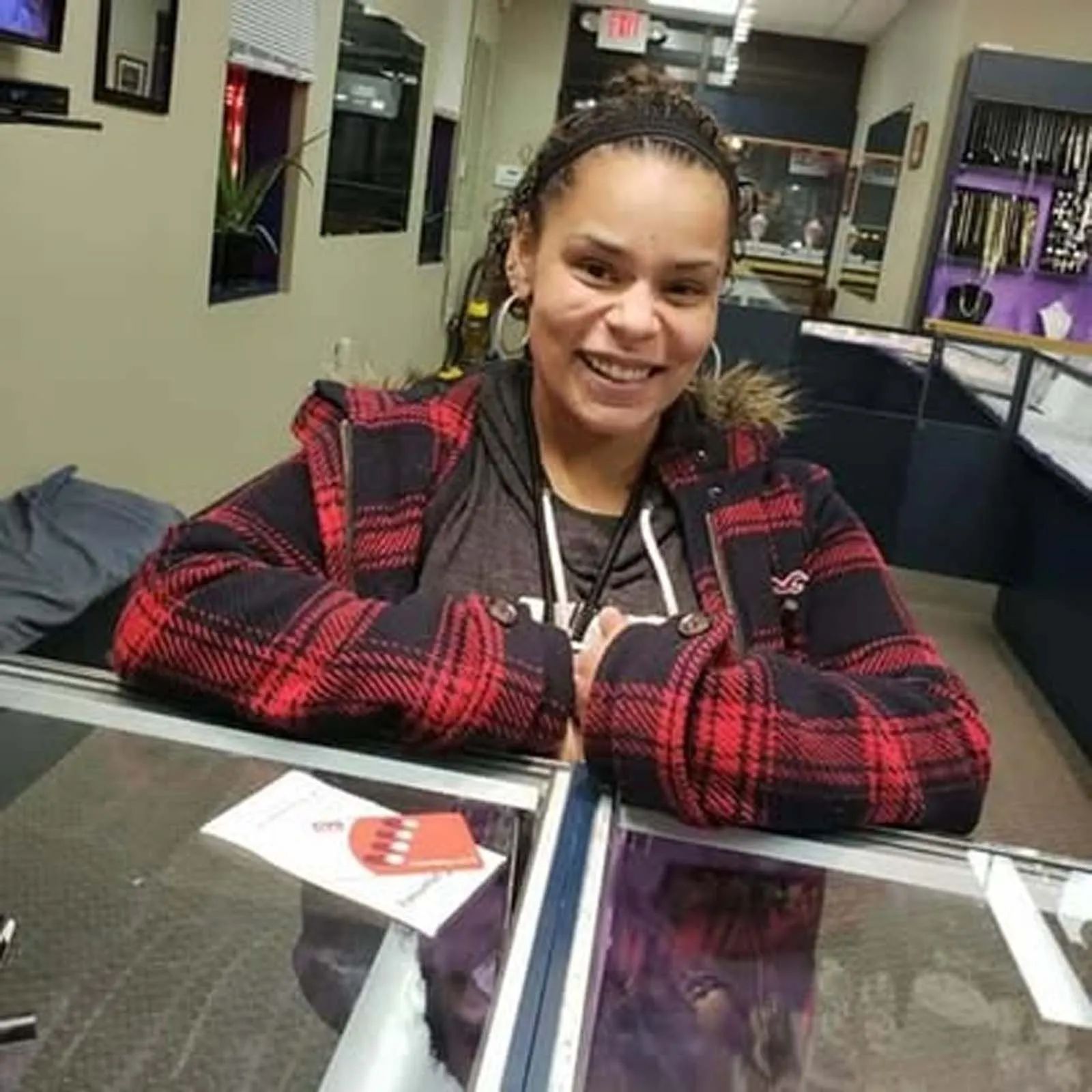 A woman in a plaid jacket is sitting at a counter in a store.