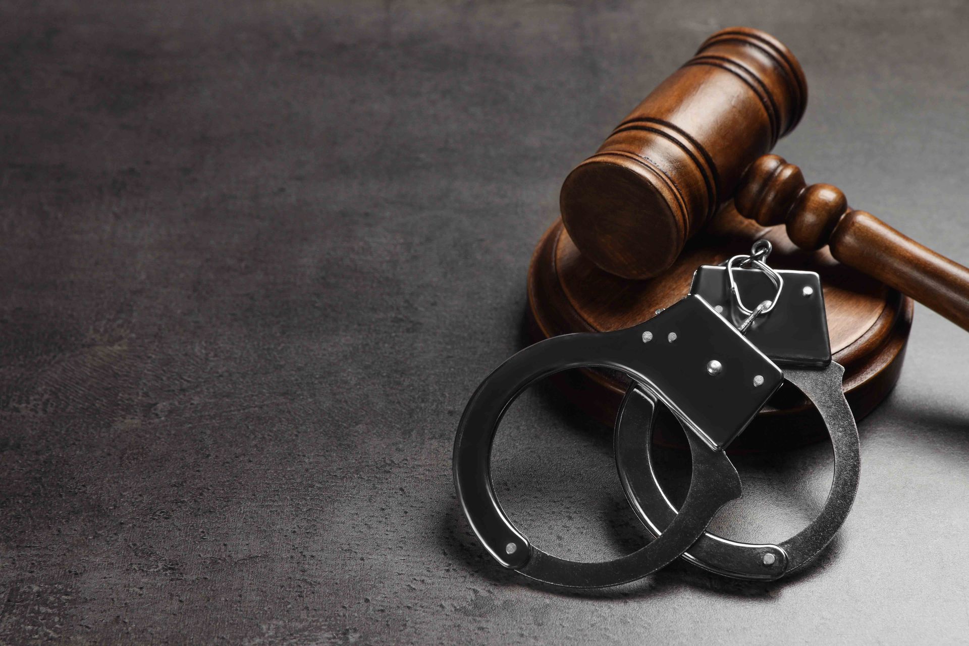 Handcuffs beside a wooden judge’s gavel on a dark surface