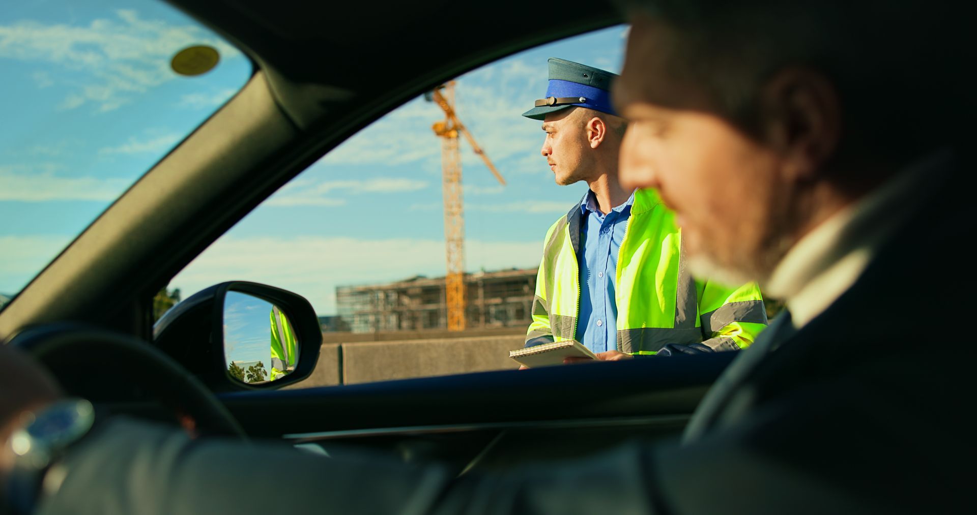 Driver stopped at roadside checkpoint, speaking with a worker in a reflective vest and blue cap.