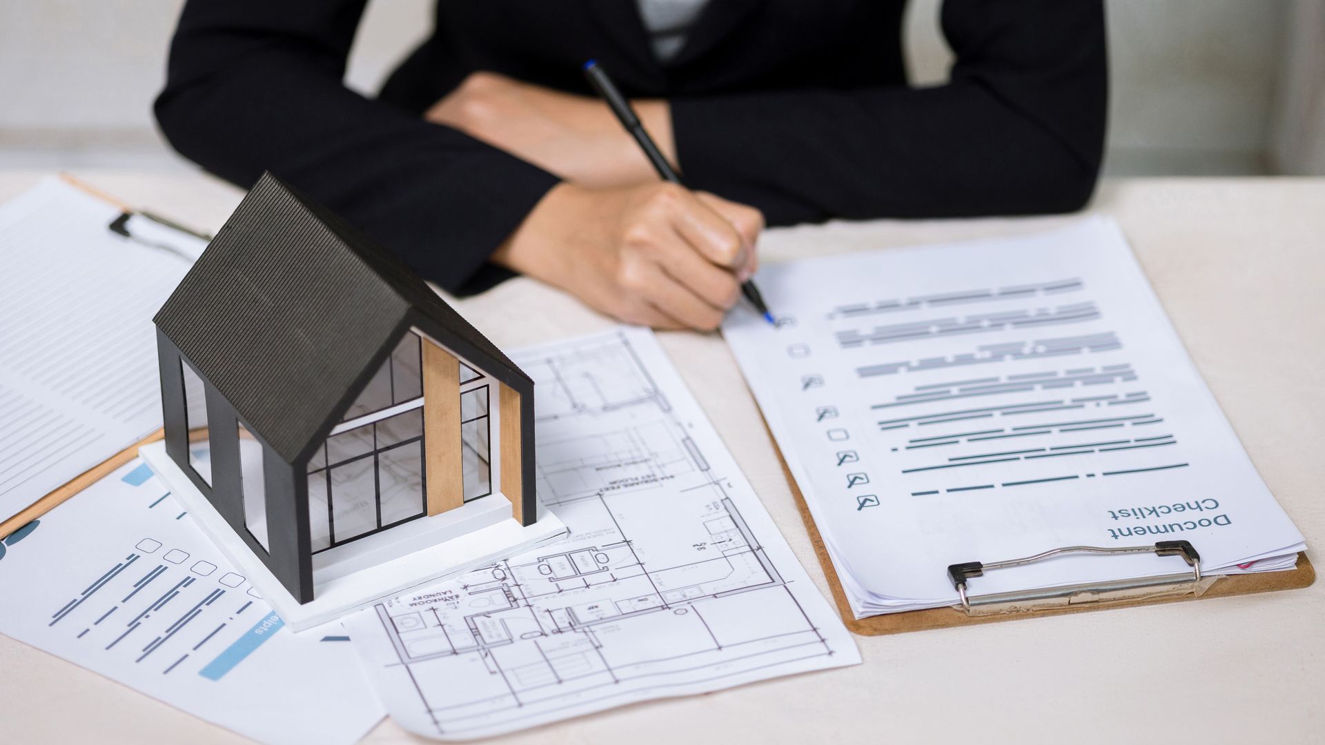 Architect reviewing house plans beside a small model home, with papers and a pen on a desk
