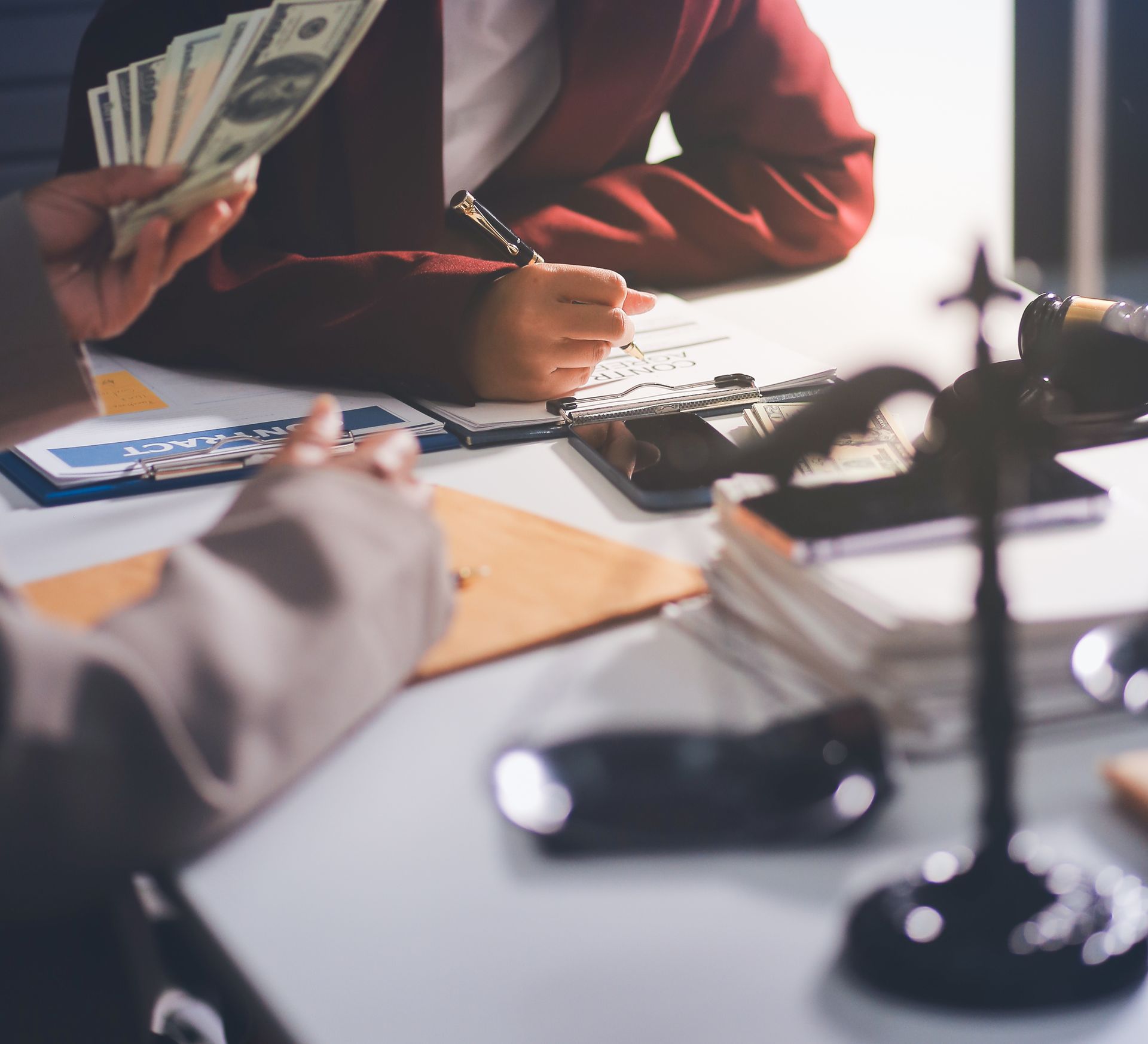 Person counting cash across a desk with paperwork, calculator, and scales in a financial office