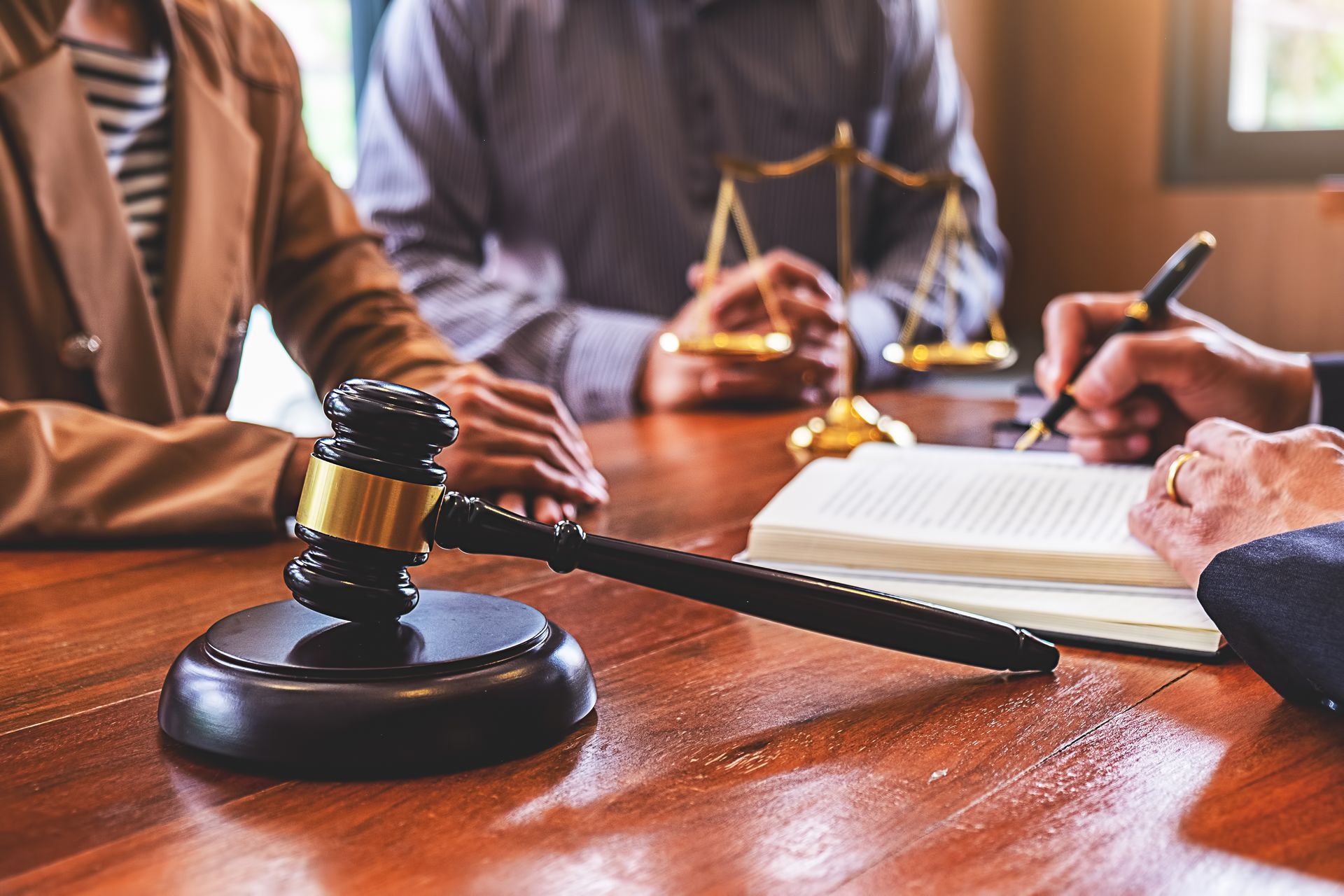 Gavel on a wooden table beside lawyers reviewing documents in a courtroom meeting