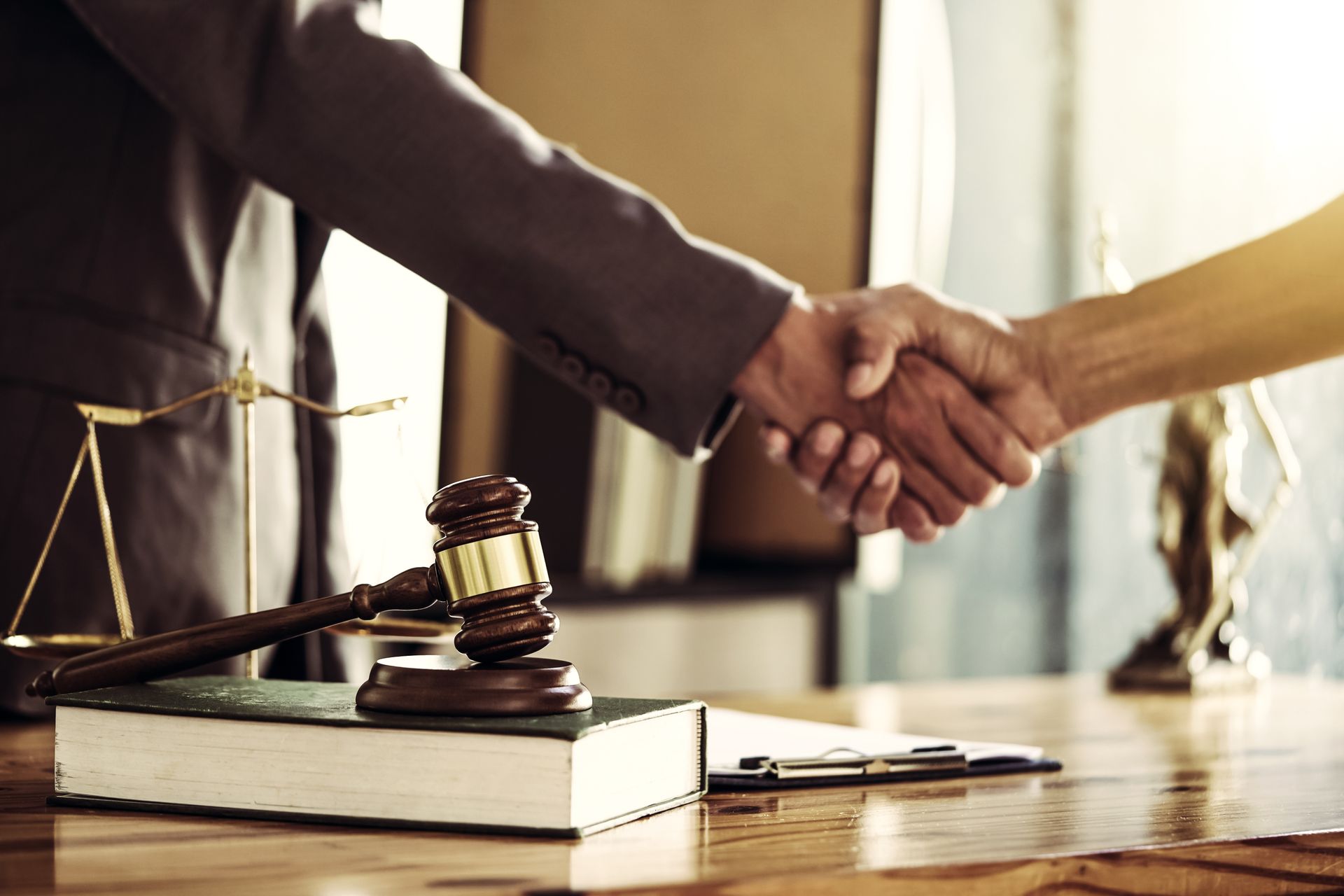 Lawyer and client shaking hands beside a gavel and legal books in a courtroom office