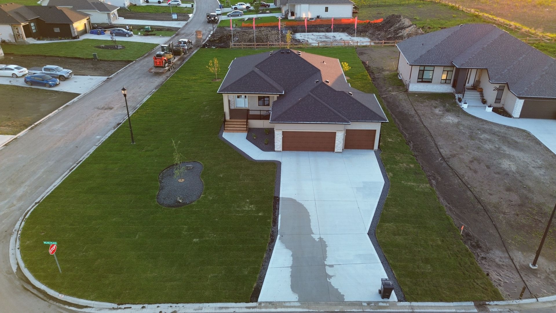 Aerial view of a new house with a driveway and green lawn; construction equipment visible in the background. new sod