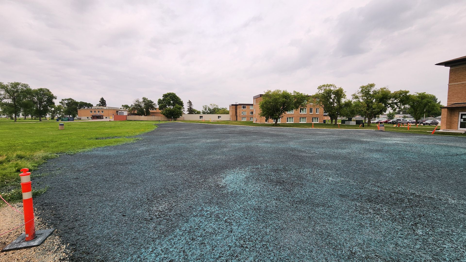 A vast expanse of blue-grey gravel transitions to green grass, with brick buildings . commercial hydro seeding