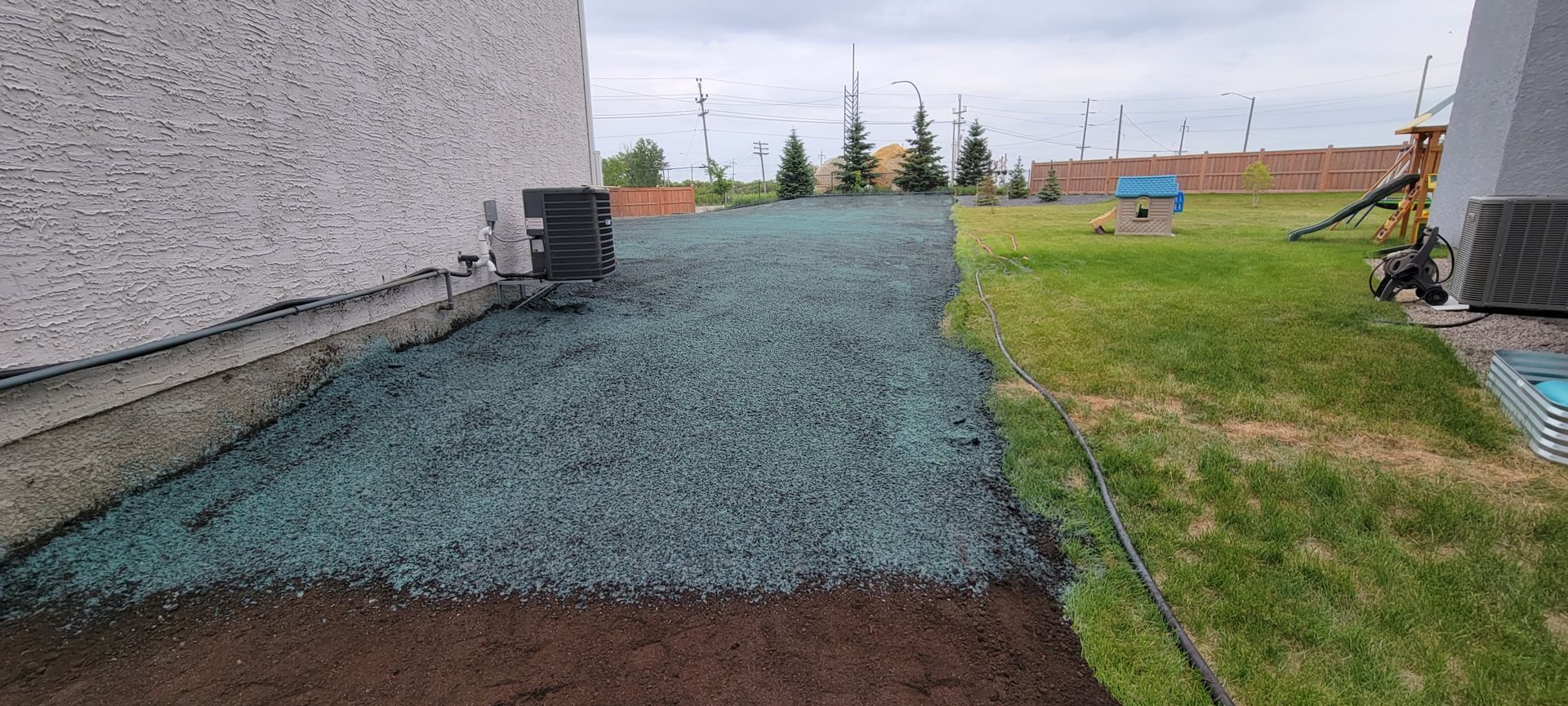 A yard with mulch on the left and grass on the right, next to a house. Cloudy sky.