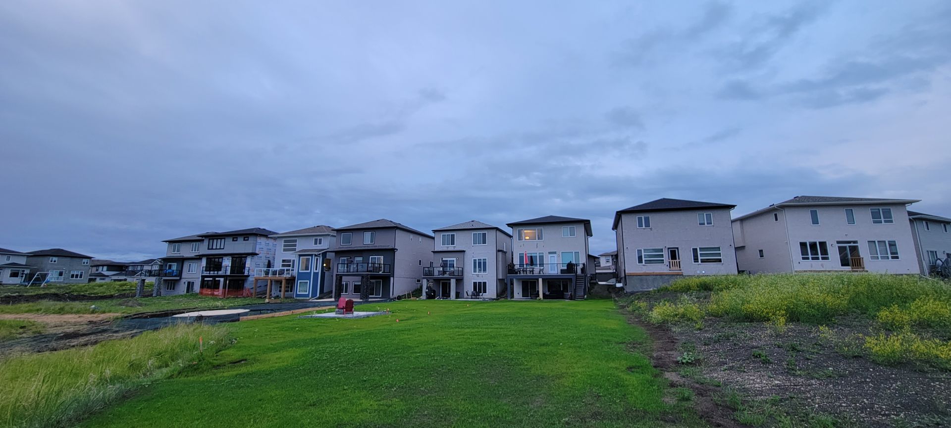 Row of modern houses with green lawn and cloudy sky.