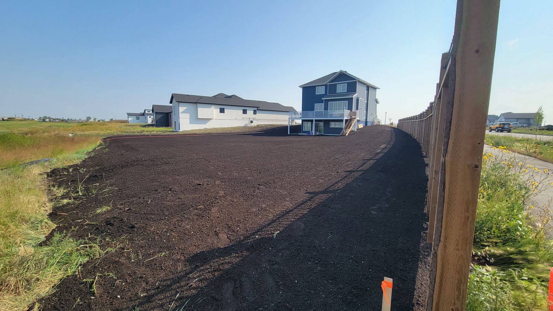 A two-story blue house on a mound of dark soil, next to a concrete barrier, new soil