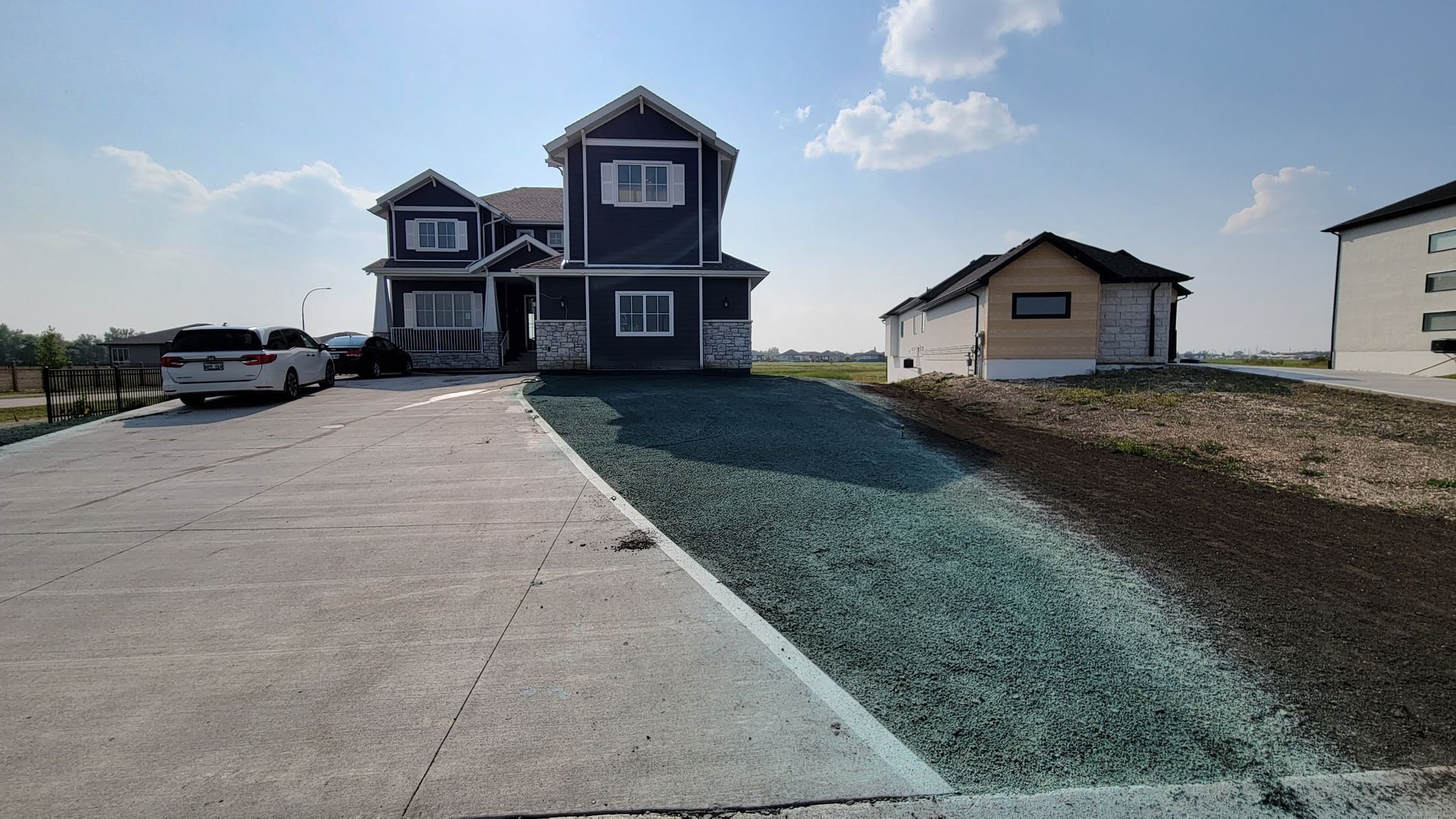Two-story blue house with white trim. Concrete driveway slopes down to a hillside. Sunny day.