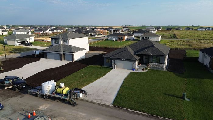 Residential construction site with houses, gravel driveways, and green lawns, some with mulch beds.