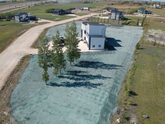Modern two-story house with trees on freshly seeded lawn; dirt road in a field.